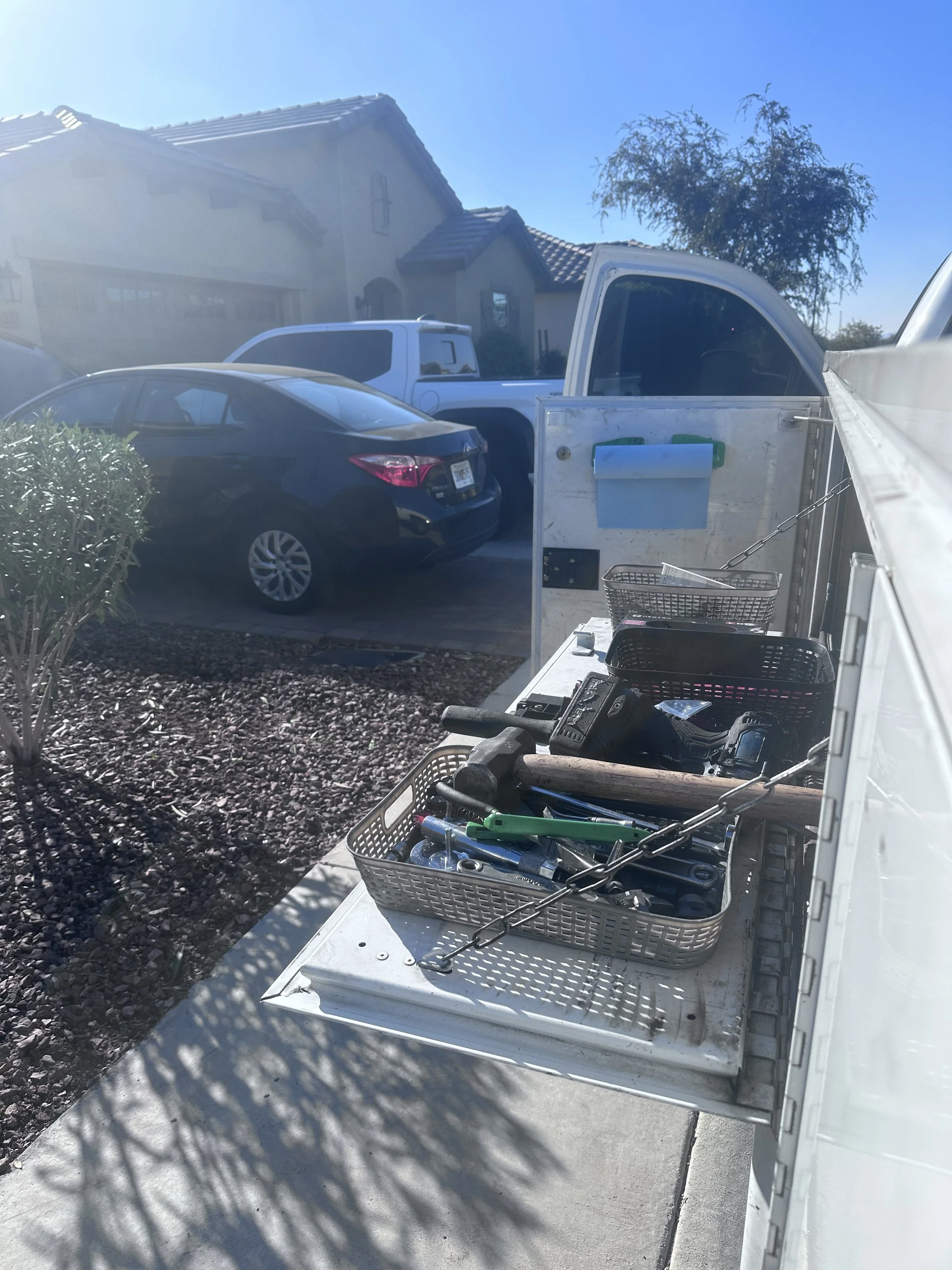 View of a front yard with several parked vehicles, a house in the background, and a work truck with tools and supplies on it.
