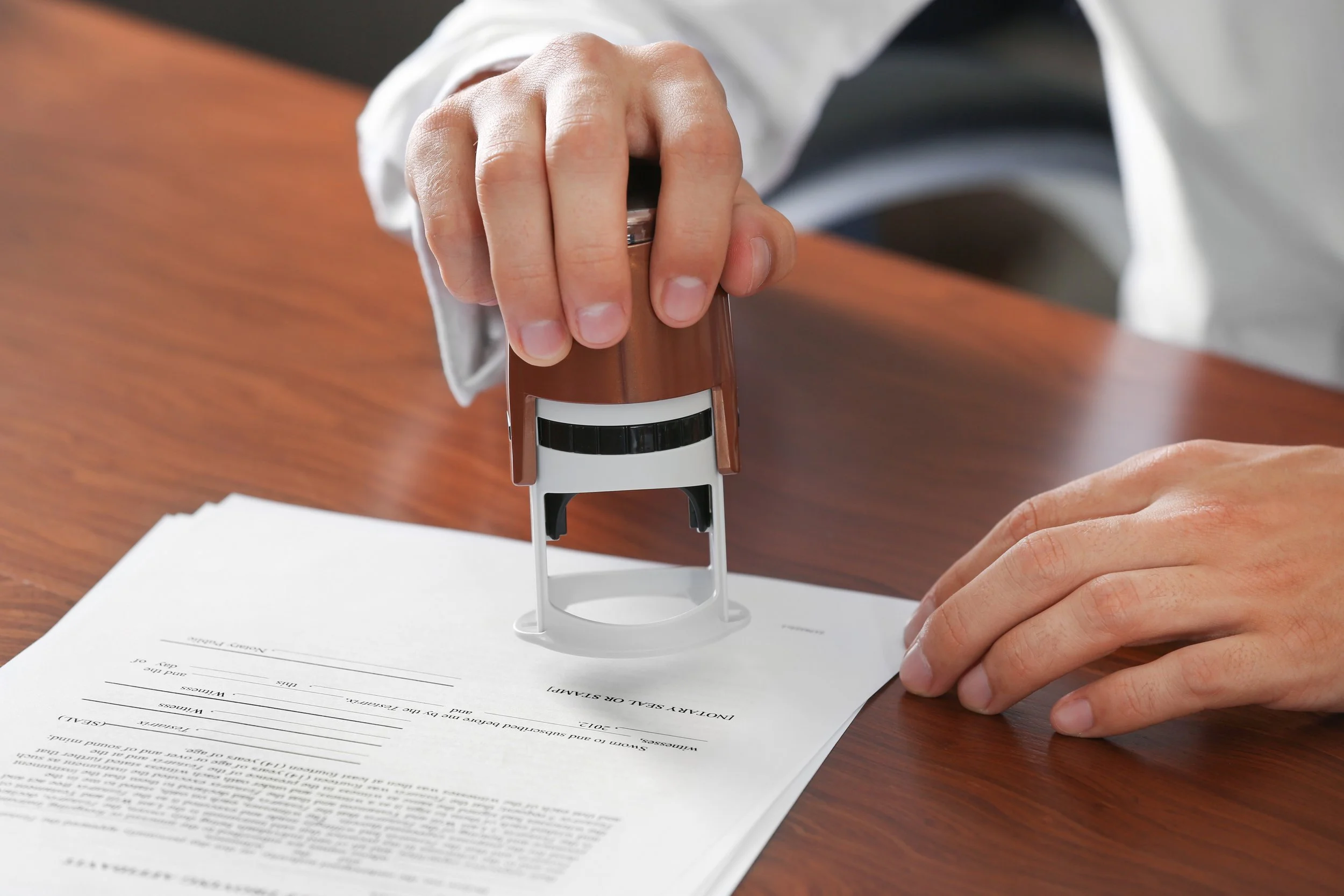 Person pressing an ink stamp onto a paper with legal document text on a wooden table.