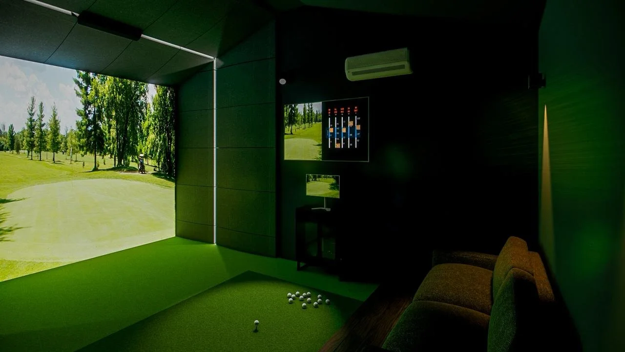 Indoor golf simulation room with a large screen displaying a golf course, a mini putting green, and golf balls scattered on the floor.