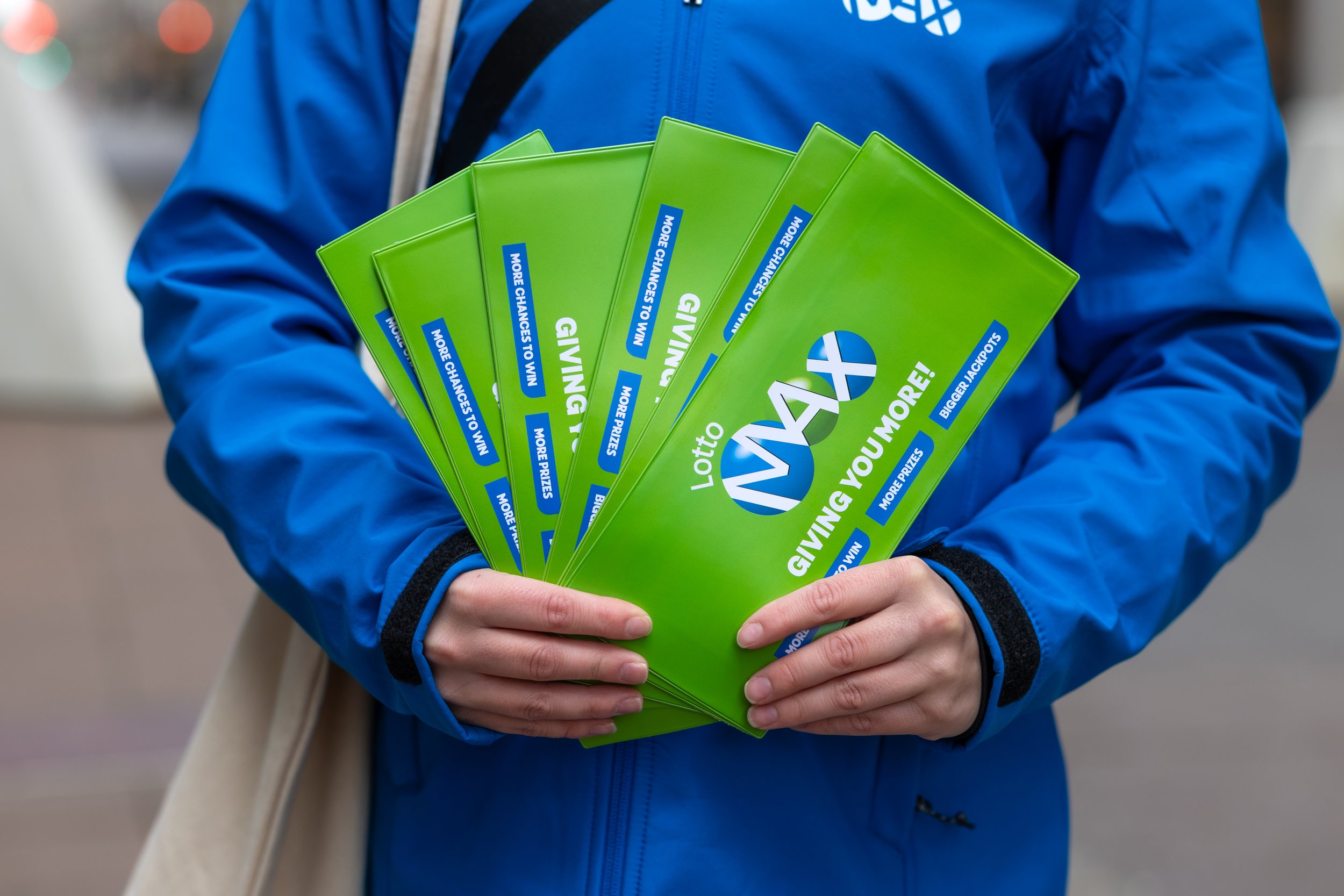 Person wearing a blue jacket holding several green lottery scratch-off tickets.