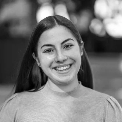 Black and white portrait of a smiling young woman with long dark hair outdoors.