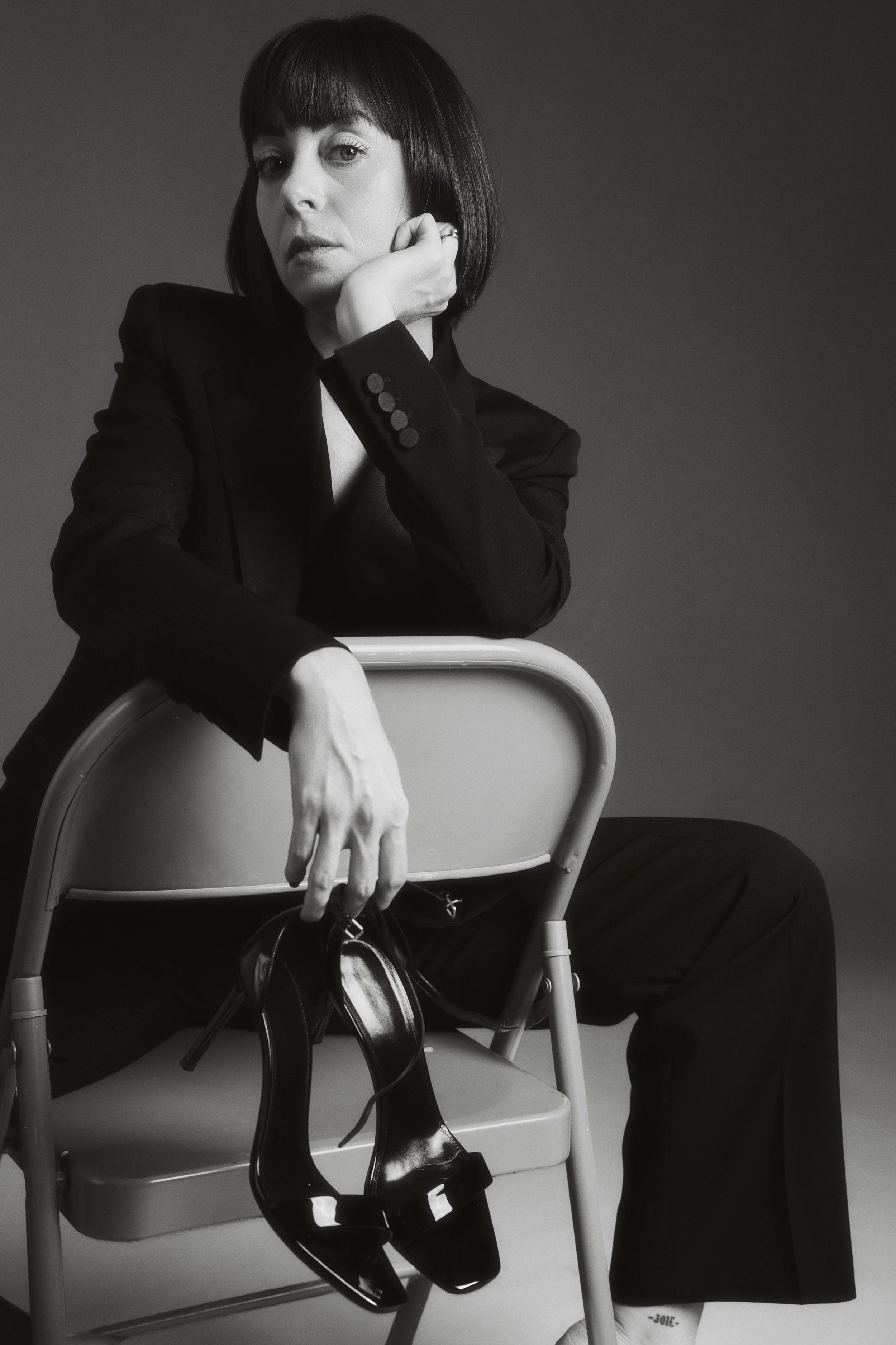 Black-and-white portrait of Sophie Valenti seated in a dark suit, holding a pair of high heels.