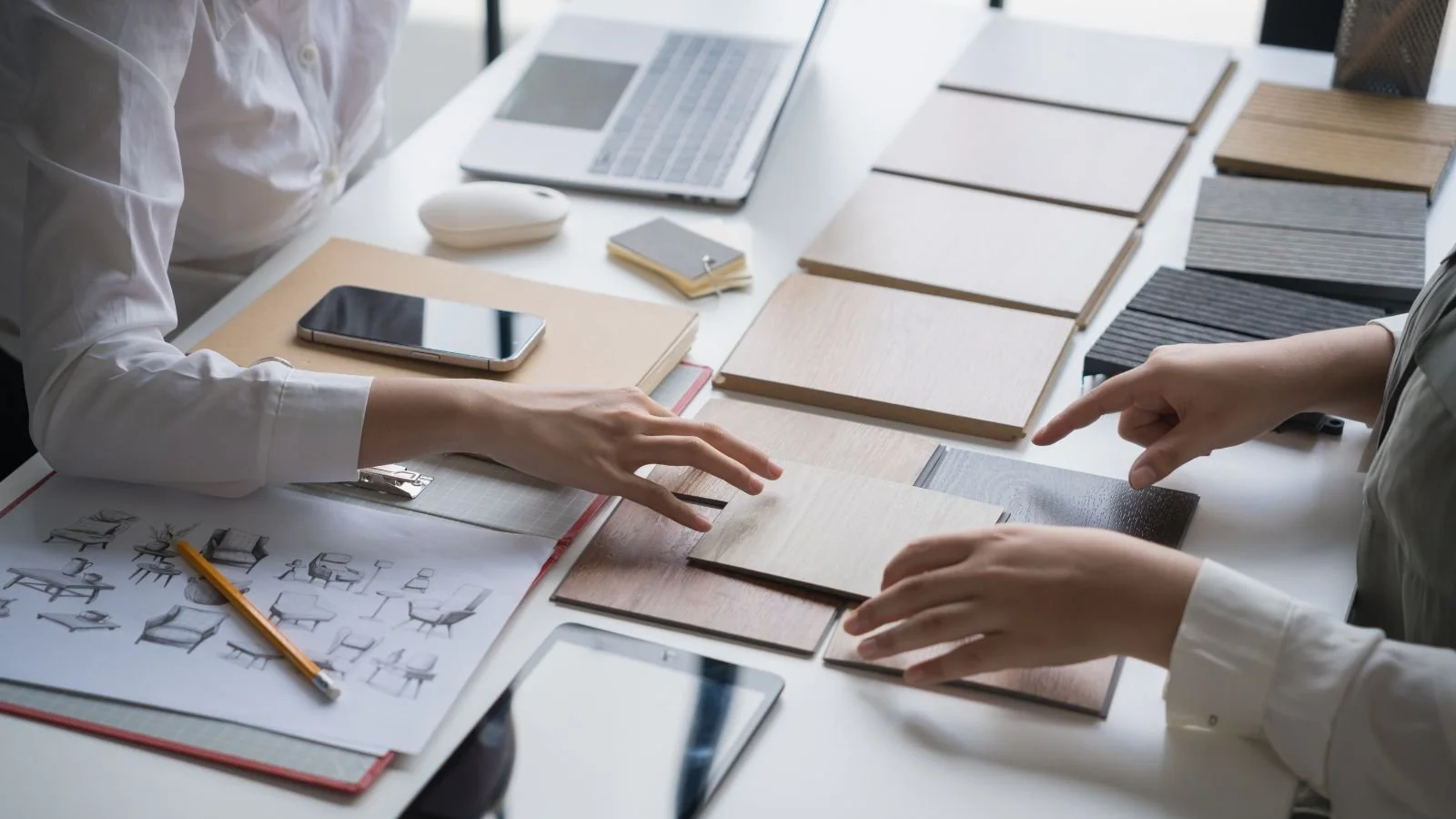 People choosing wood and fabric samples for furniture or interior design at a workspace.