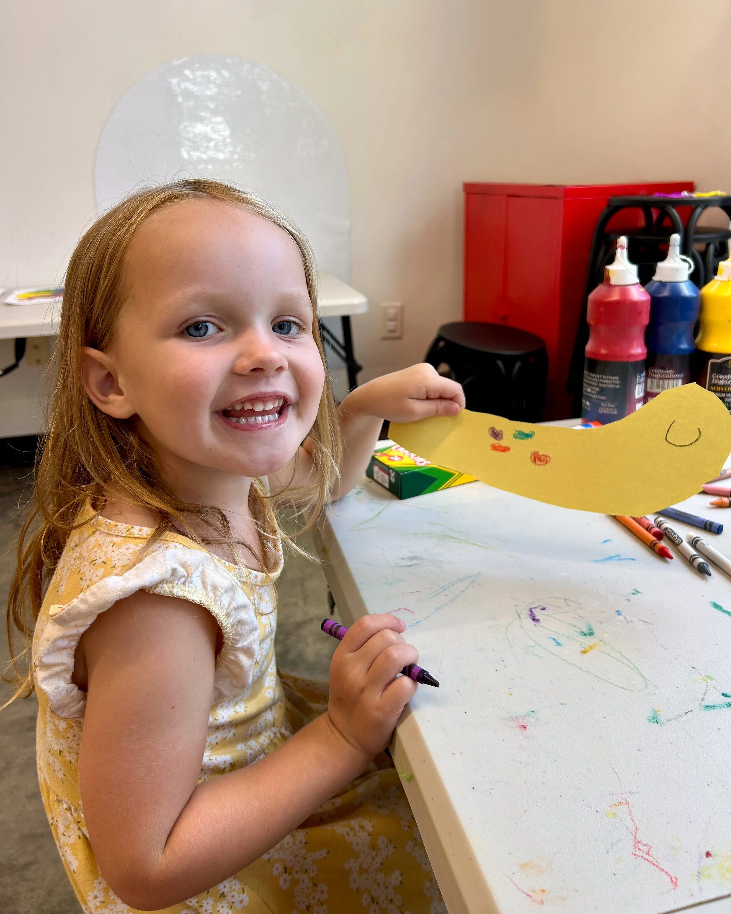 A little girl smiles and holds a yellow snail she is coloring