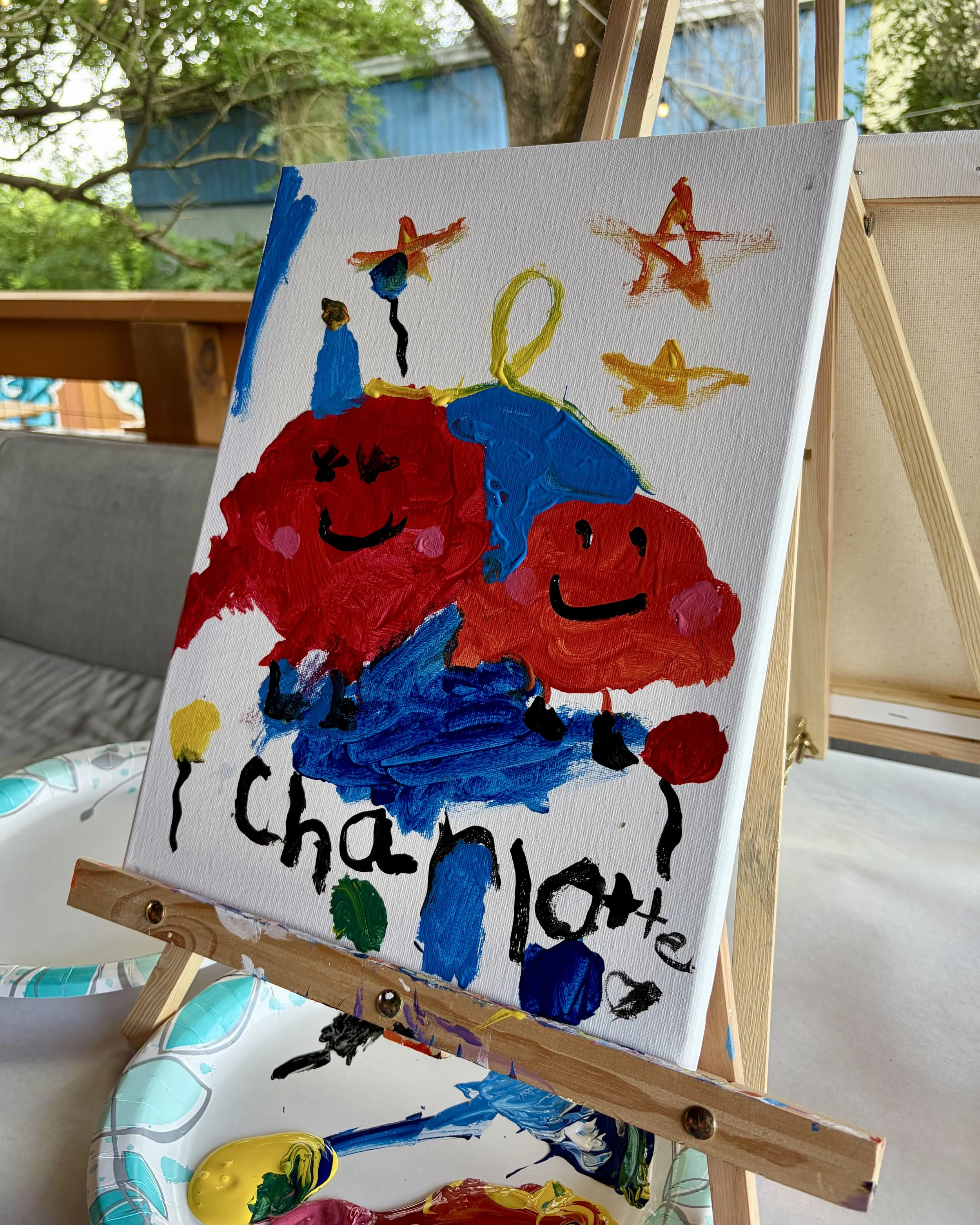 Close up of a tomato painting with stars on an easel done by a child and signed with their name