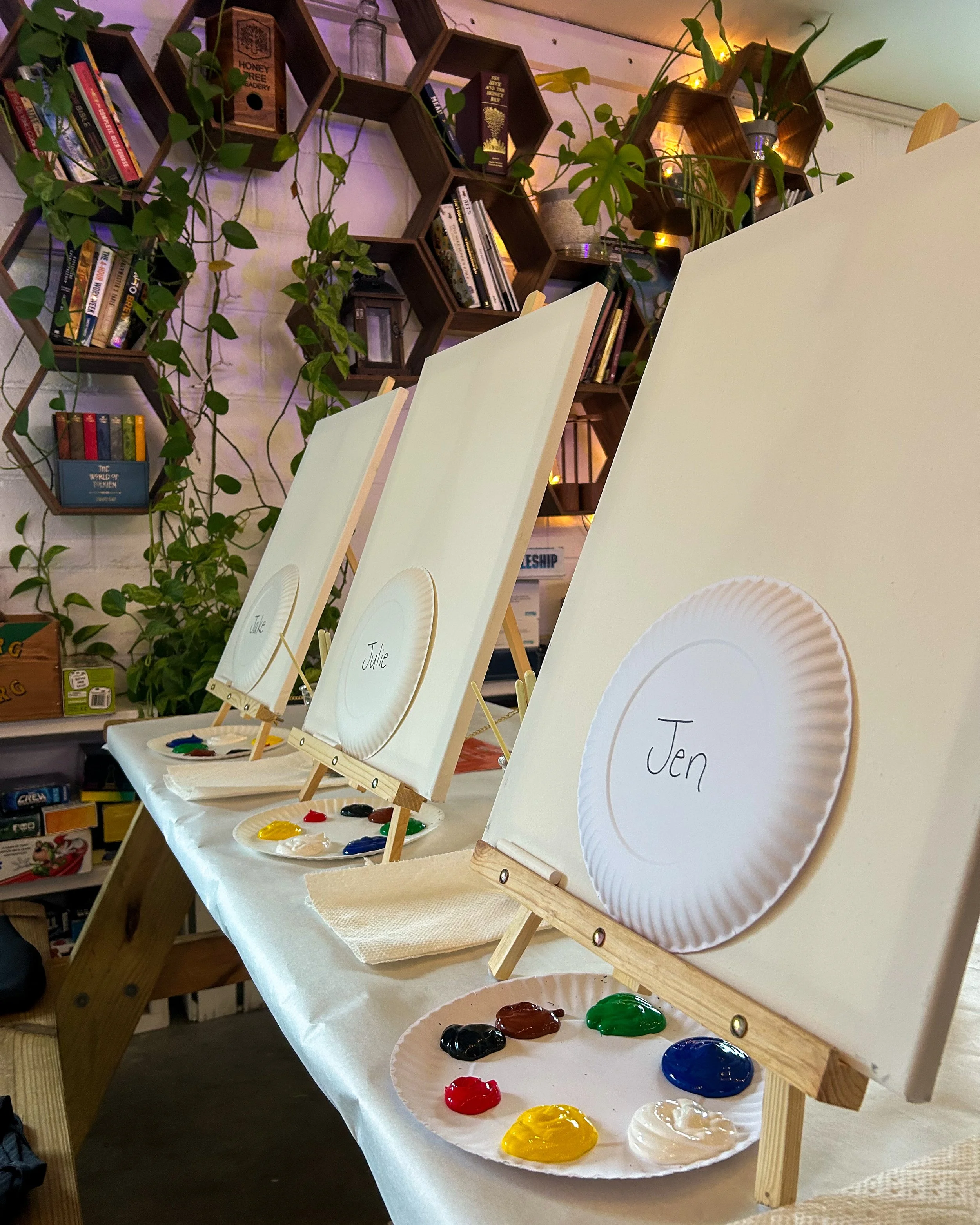 Up close photo of three blank canvases with paper plates with names on them and fresh paint