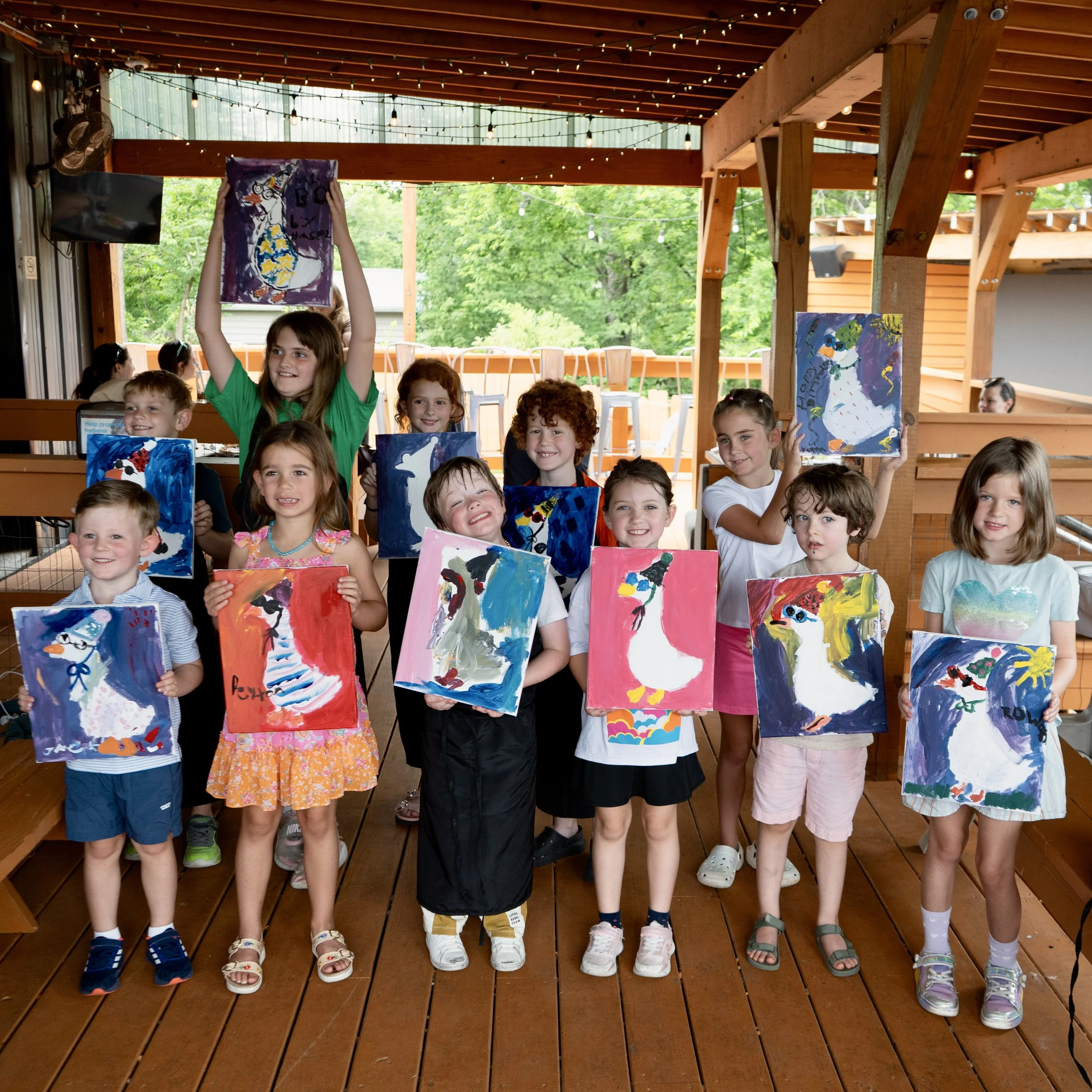 Group of young children proudly displaying colorful paintings of geese