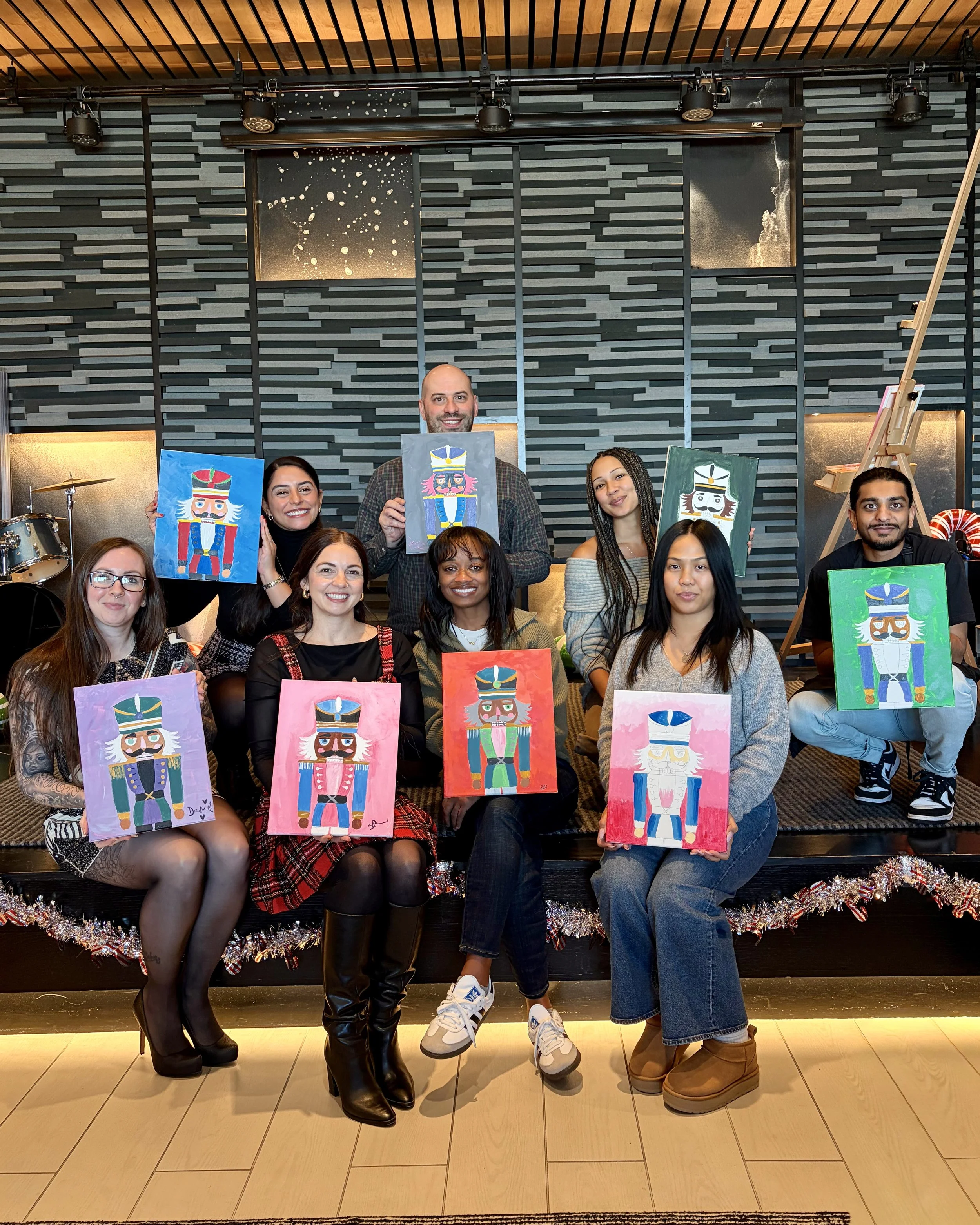A group of people sits on stage at a private event with colorful nutcracker paintings they finished