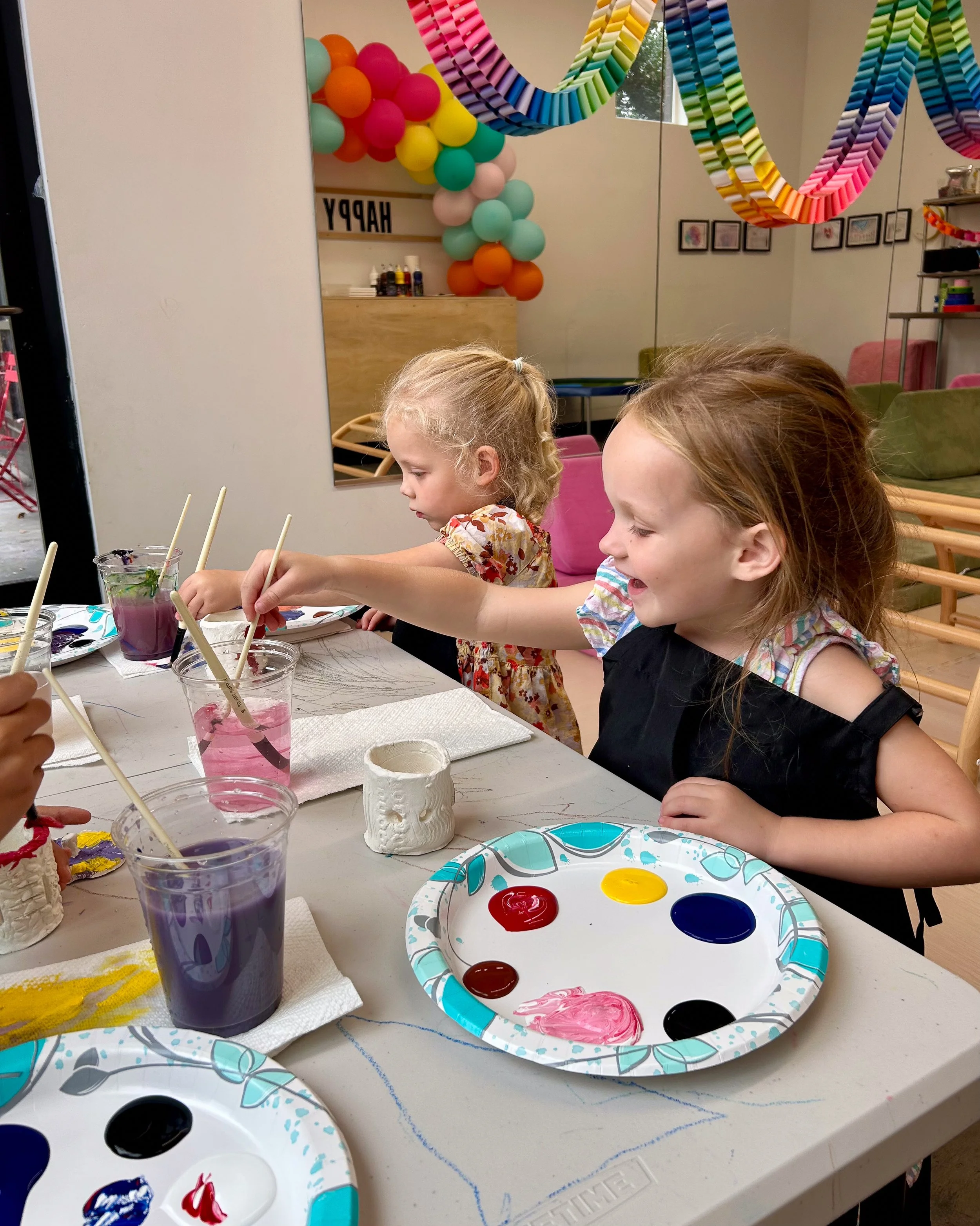 A group of students works on painting their clay candle holders with a big smile