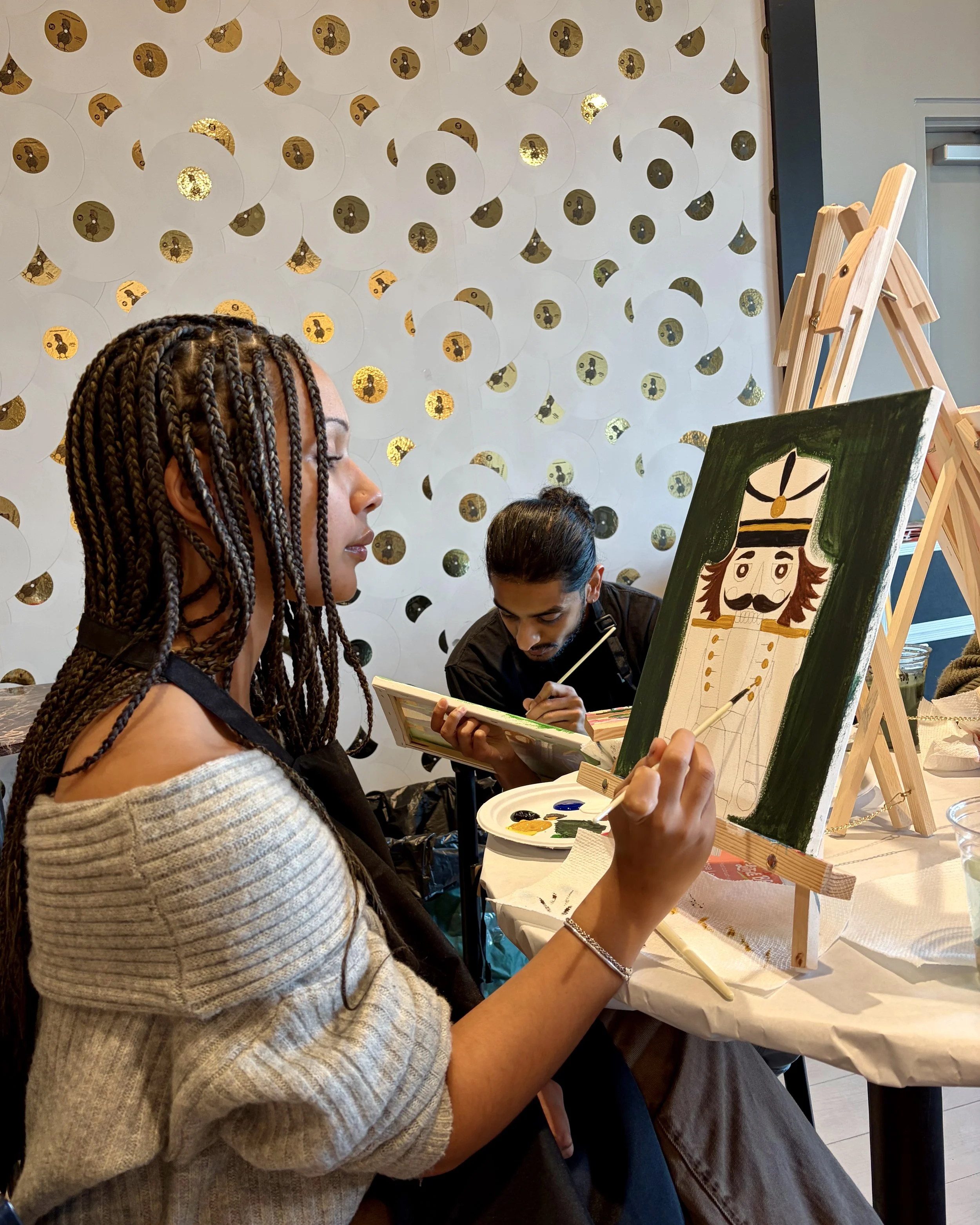 A woman with braids paints a green nutcracker painting