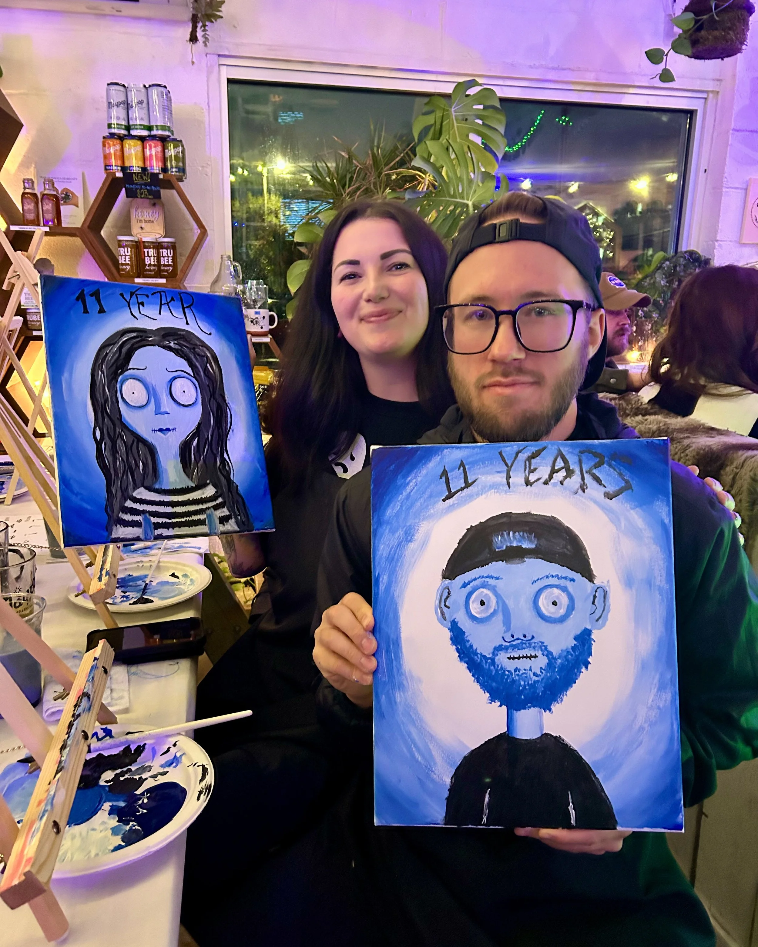 A couple poses with their finished spooky self portraits on date night