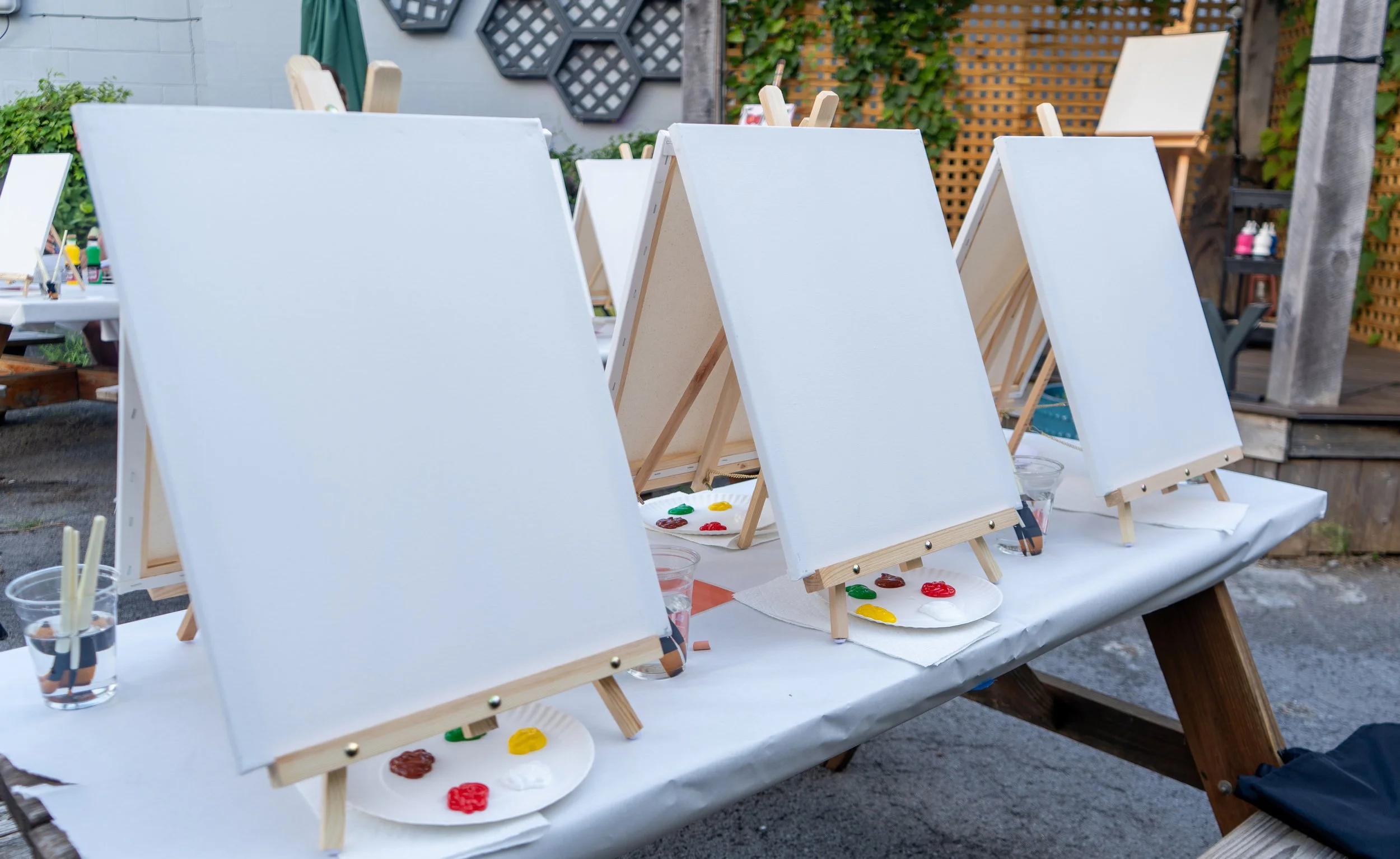 A series of three blank canvases sit in a row with paint and paintbrushes