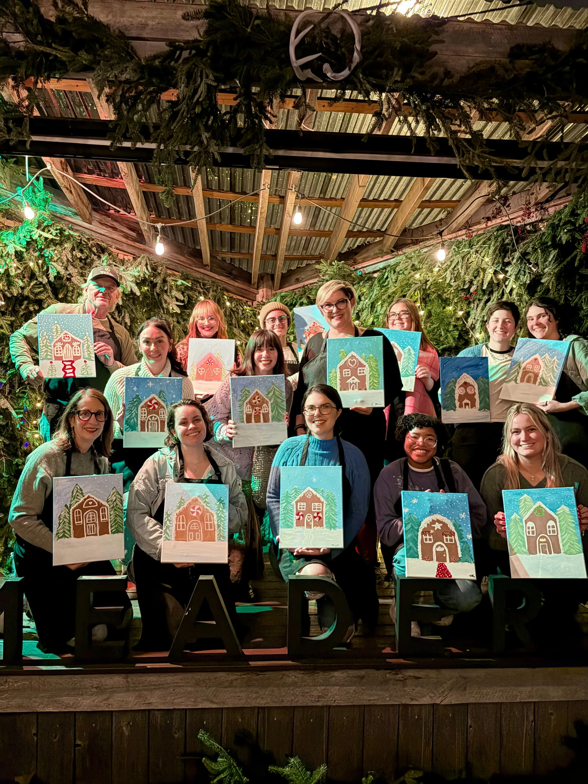 Group of people holding up their gingerbread house paintings on stage