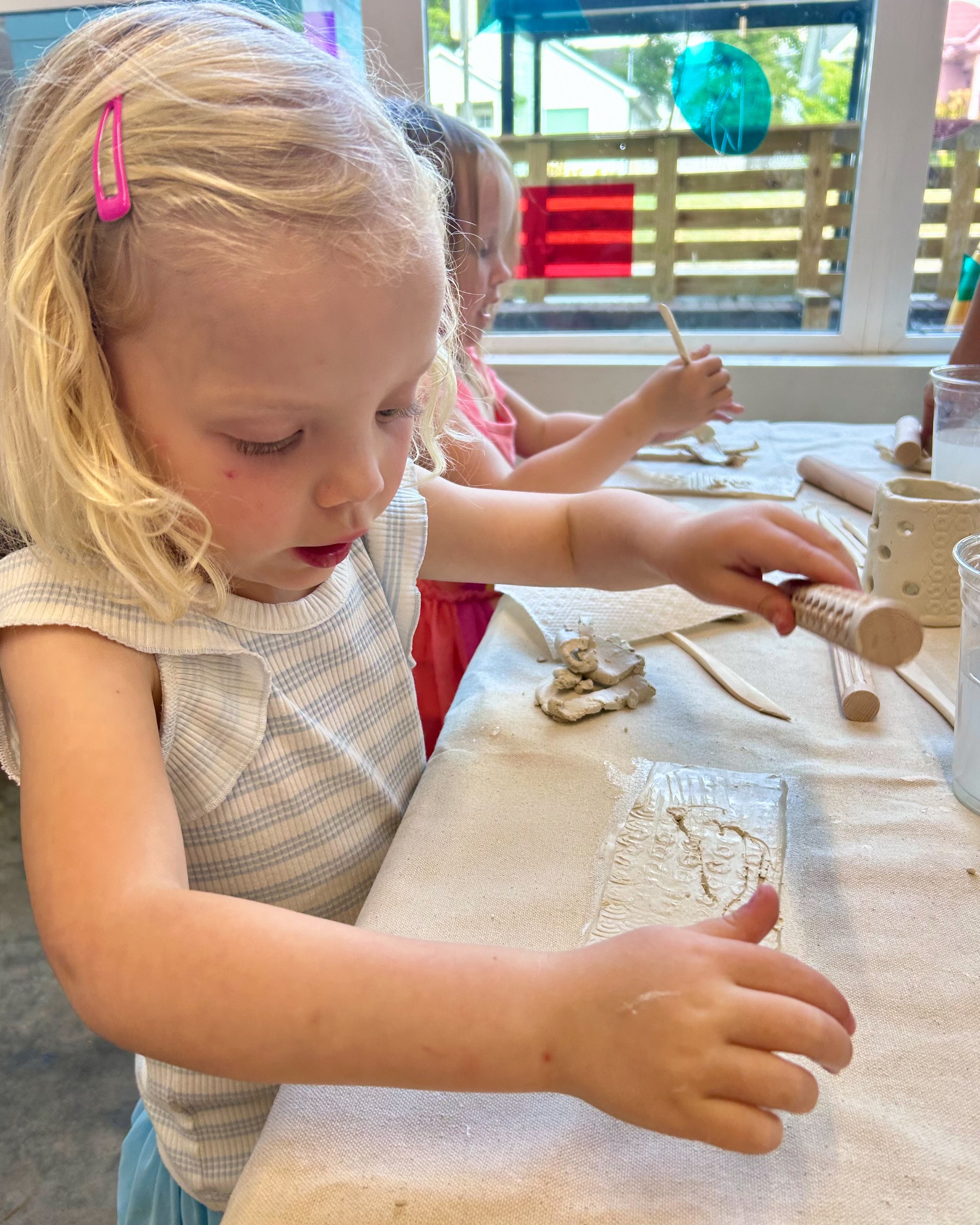 A little girl practices rolling out clay