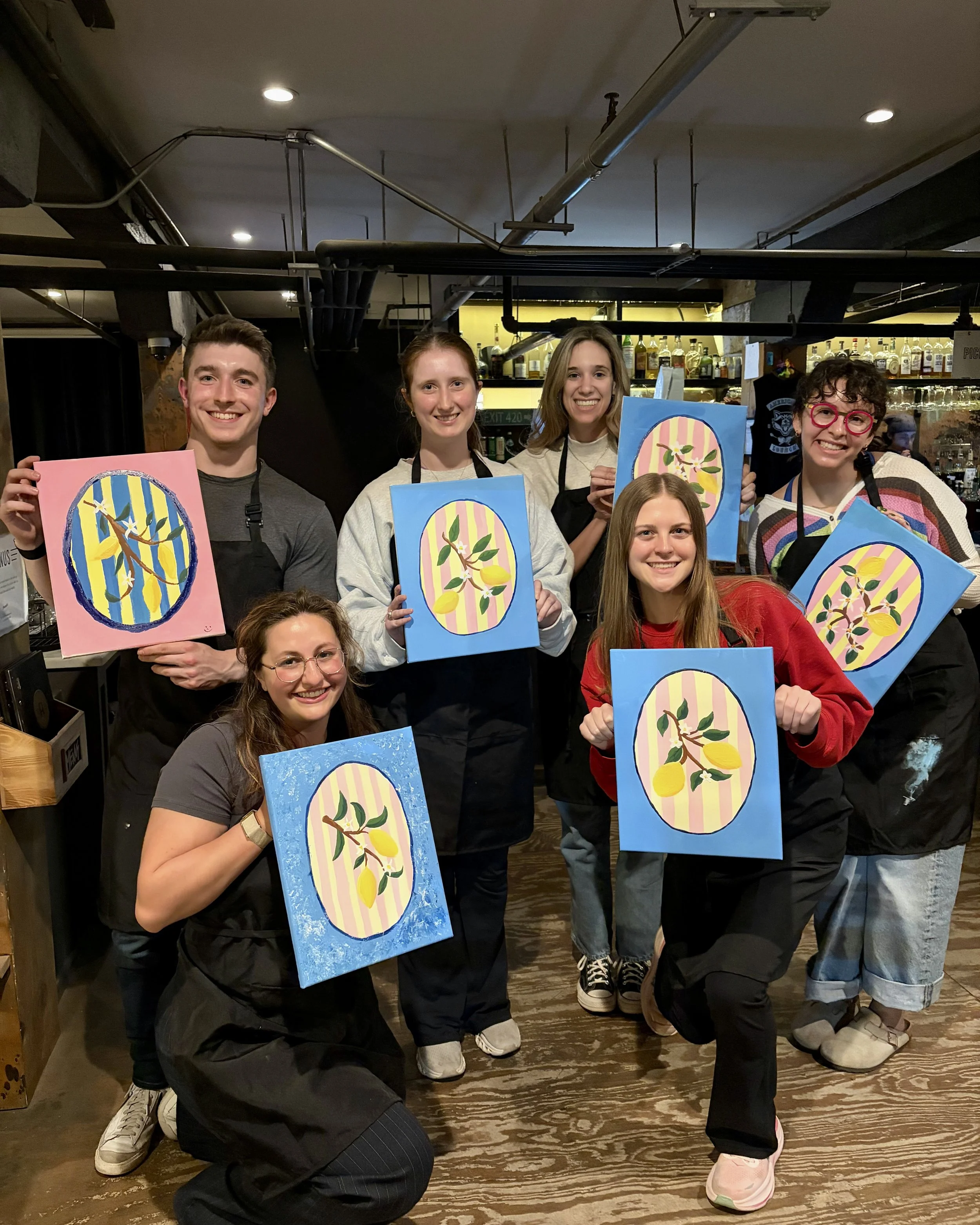 A group of people pose in a coffee shop with their finished lemon paintings