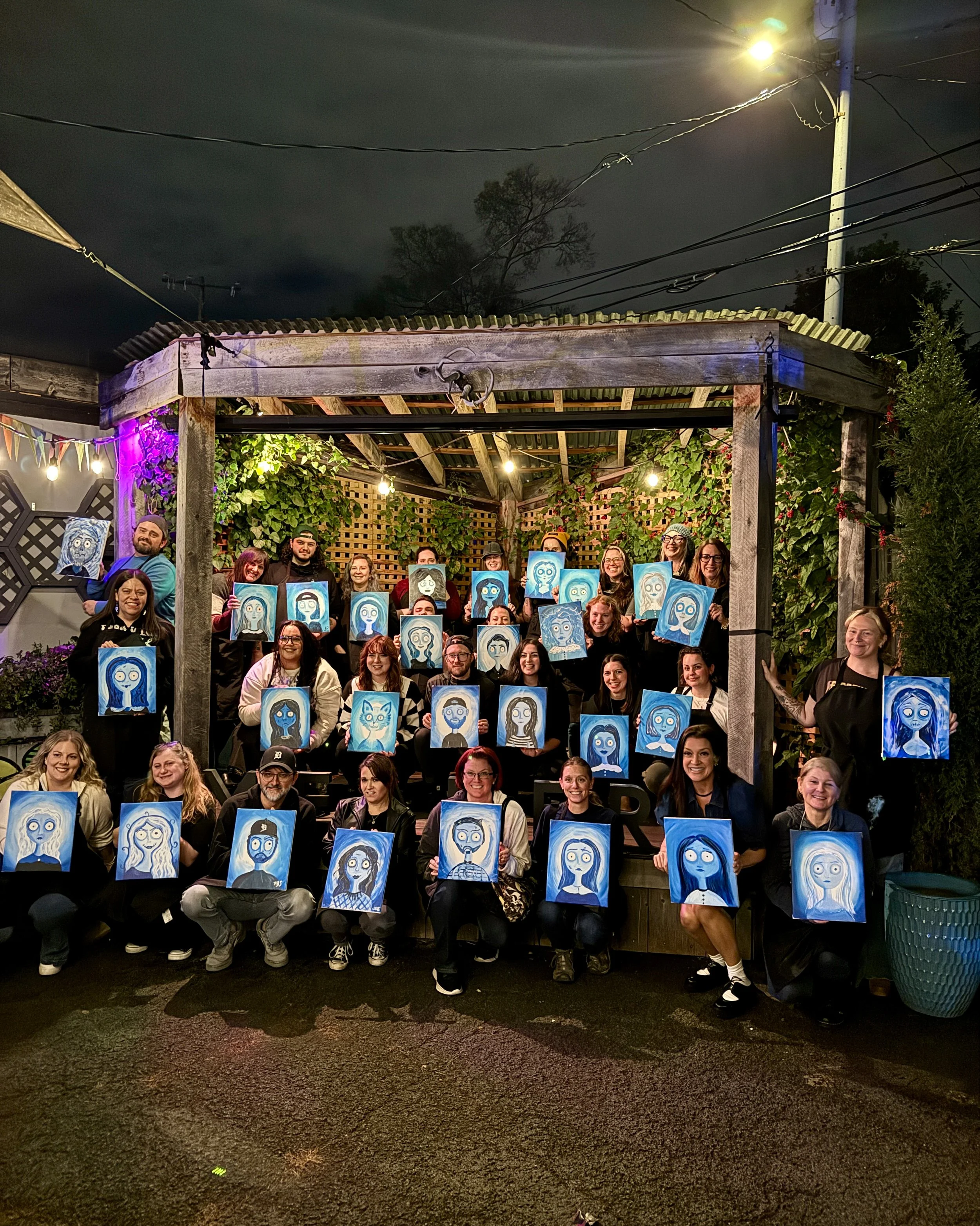 Large group of people holding spooky self portrait paintings on stage at night