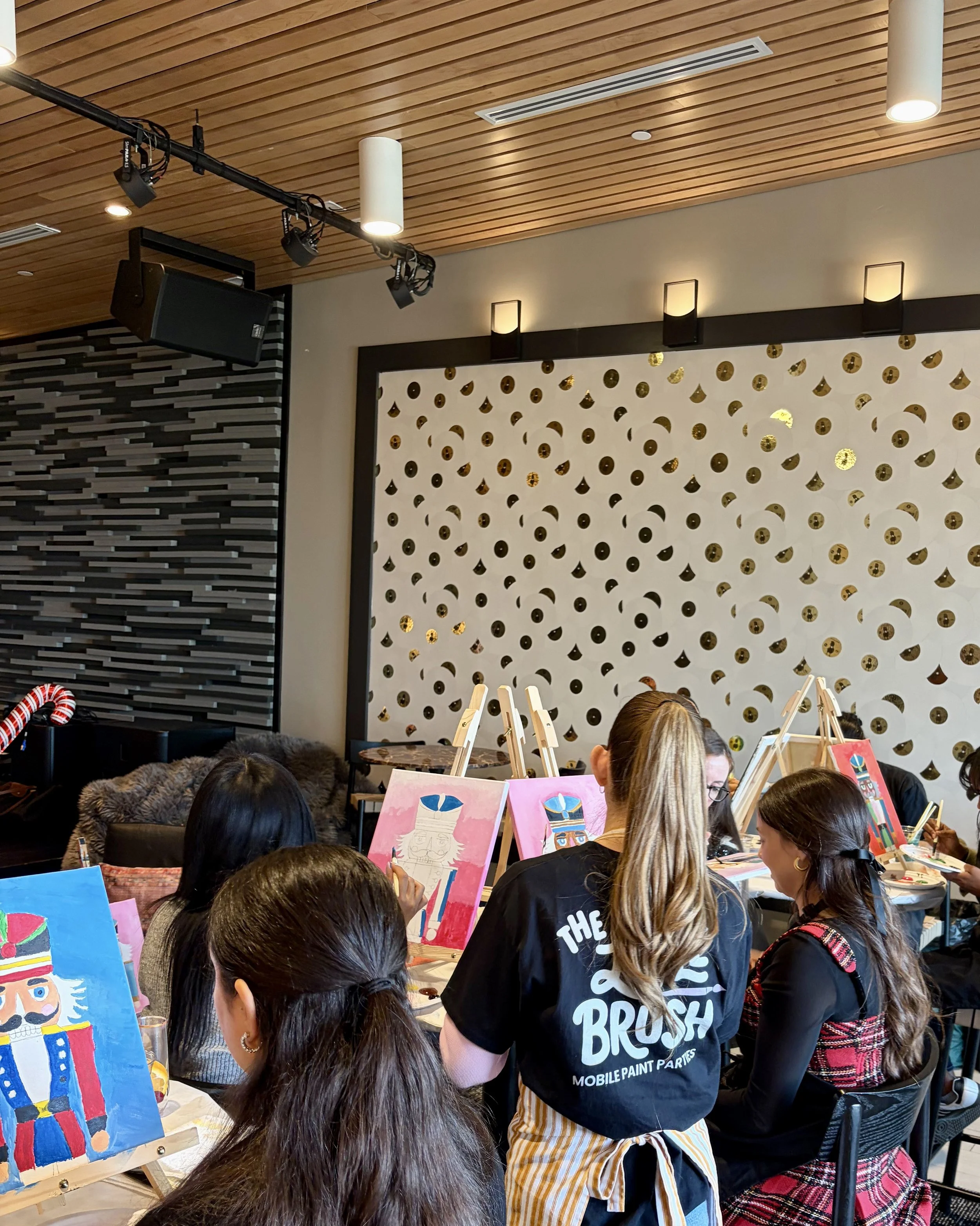 The back of an instructor in a Little Brush shirt helping a student with their nutcracker painting
