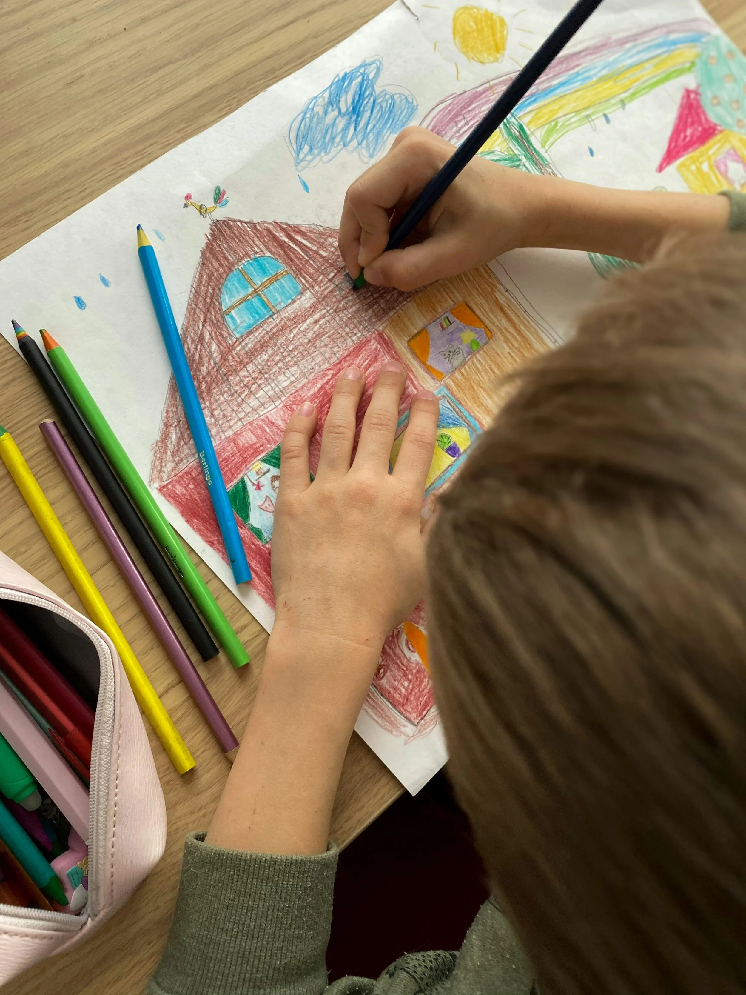 Student drawing a house with colored pencils