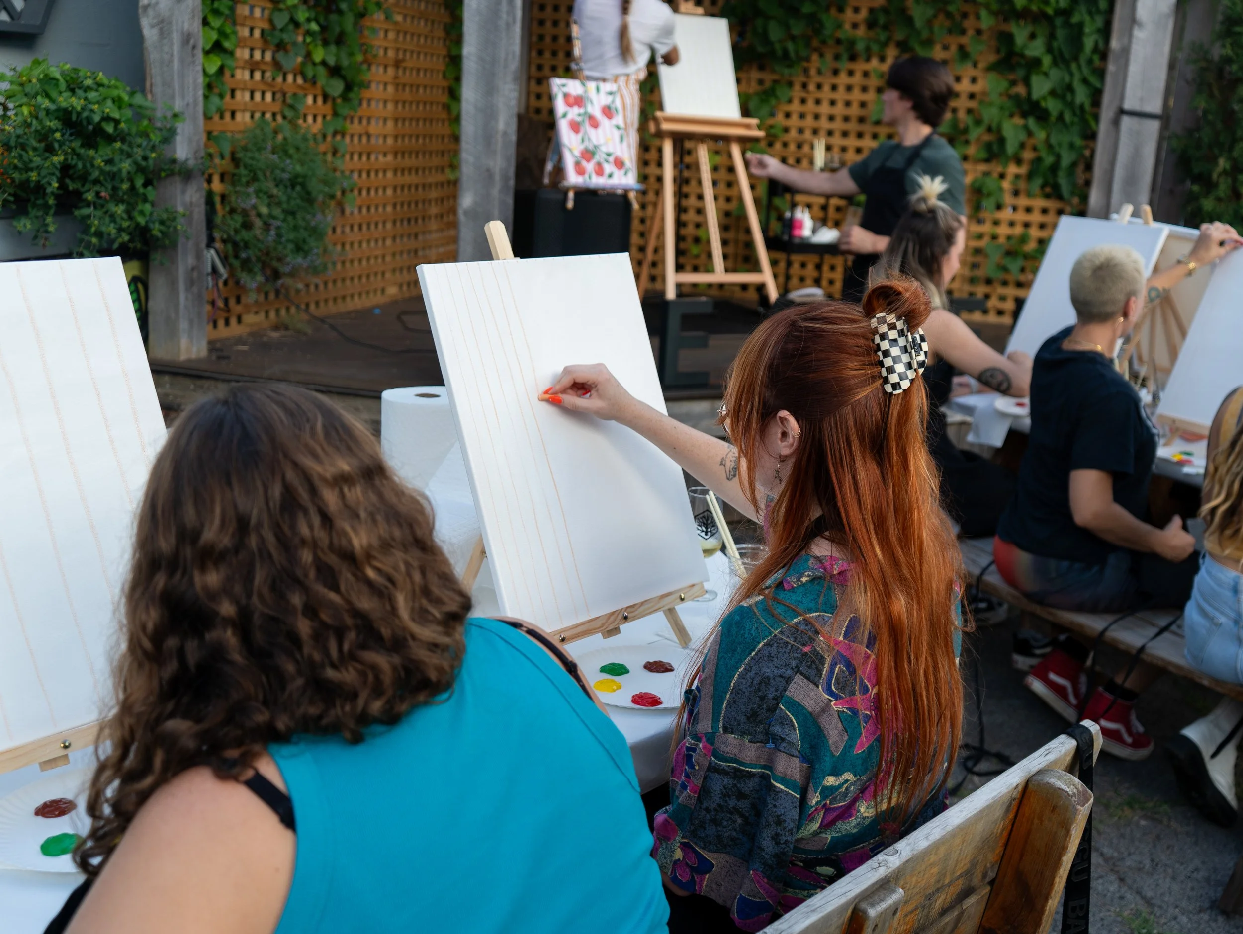 A girl with brown hair and a girl with red hair and a claw clip drawing on a canvas 