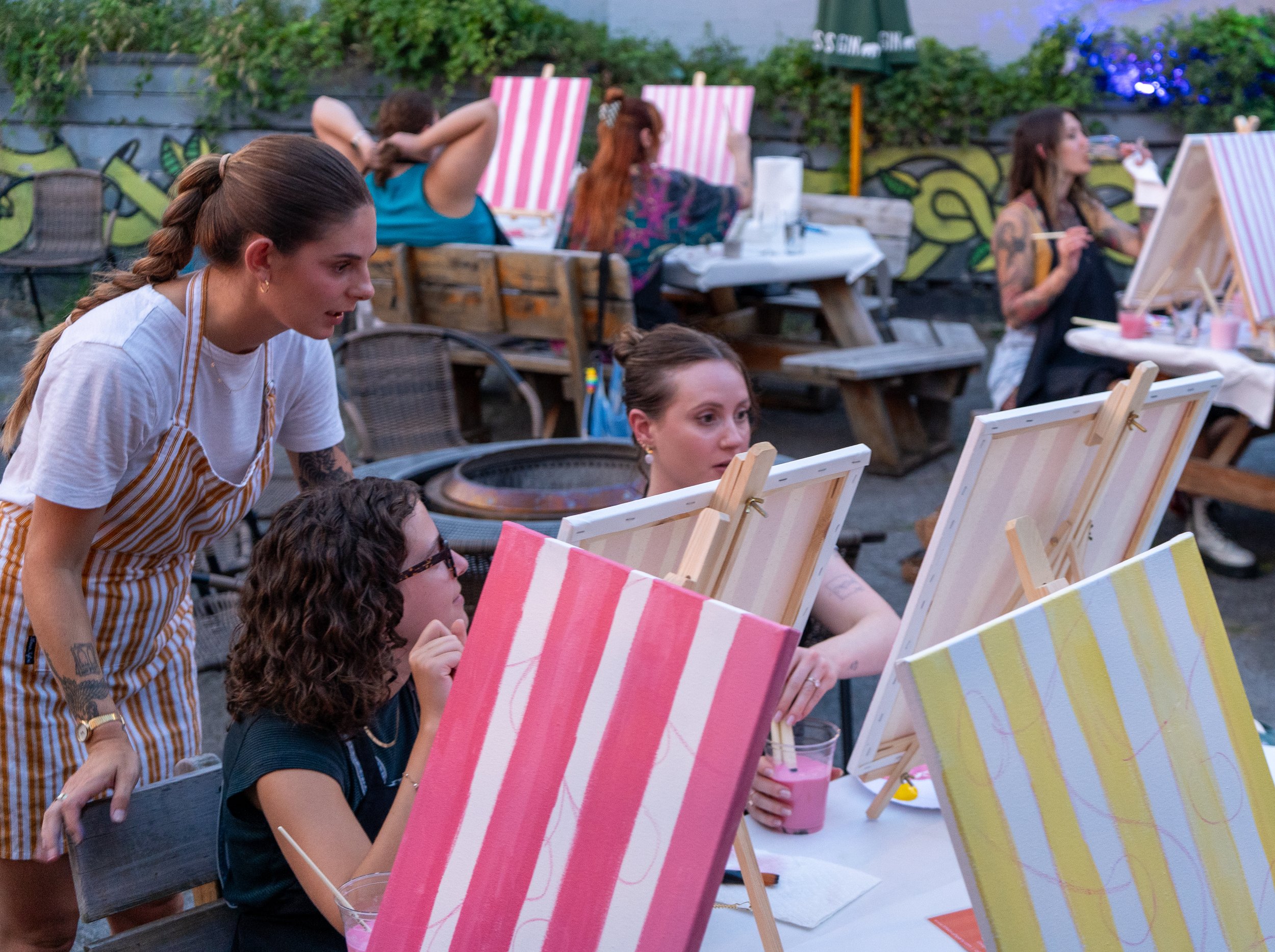 An instructor with a braid helps two women with their stripe paintings