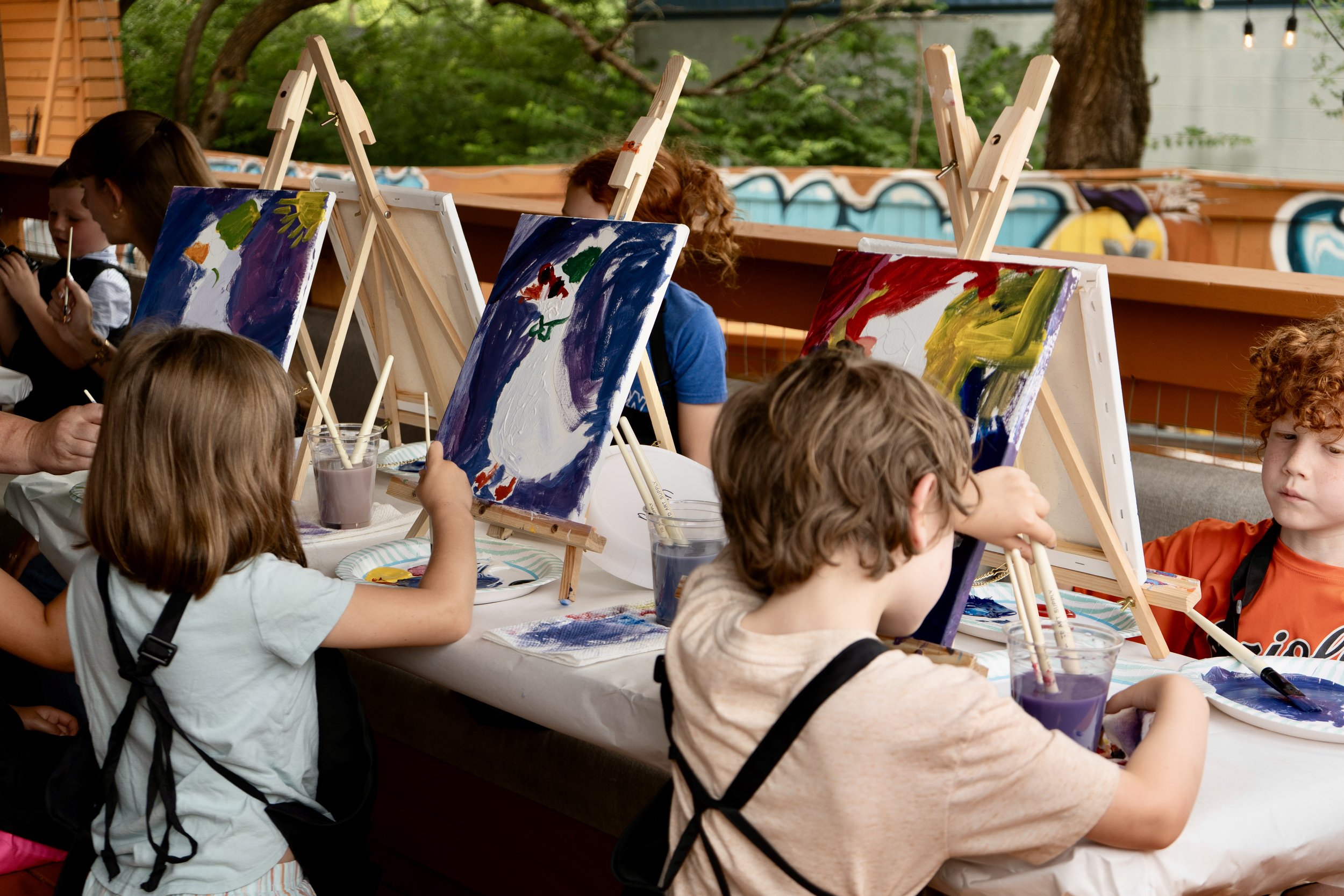 A group of kids paints colorful geese together on a patio