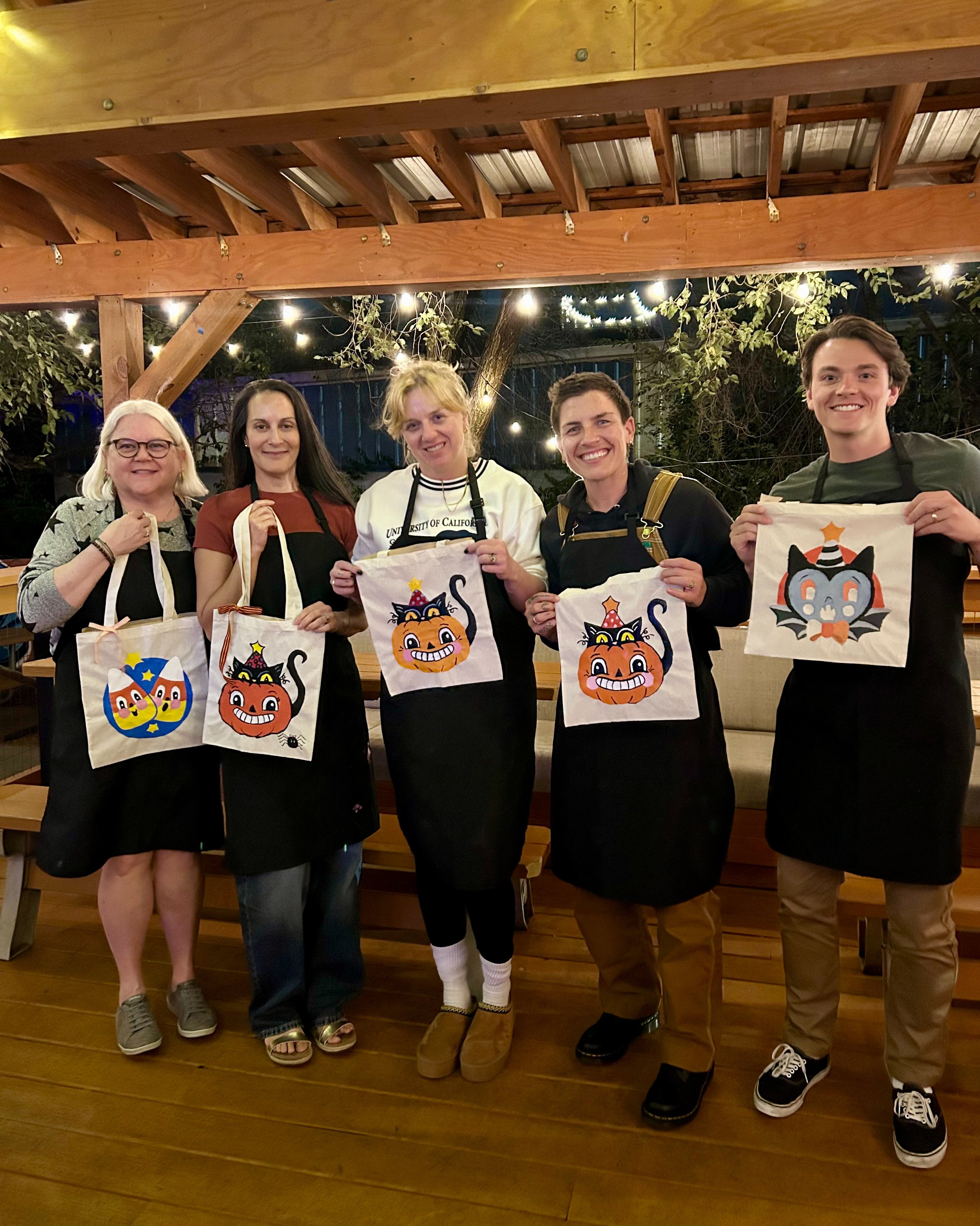 Group of painters on a patio holding tote bags with Halloween art