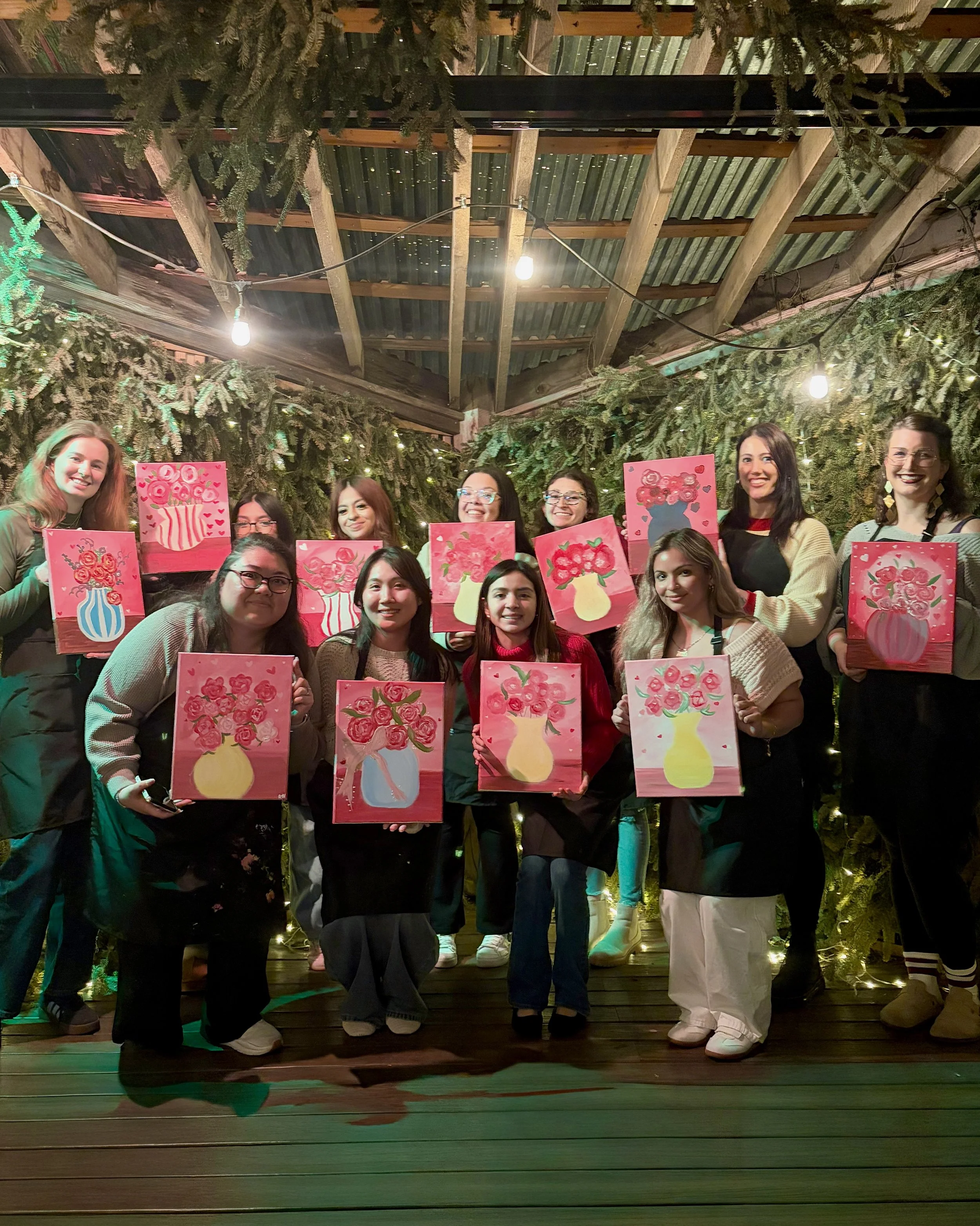 A group of women poses on stage with their finished bouquet paintings on Valentine's Day