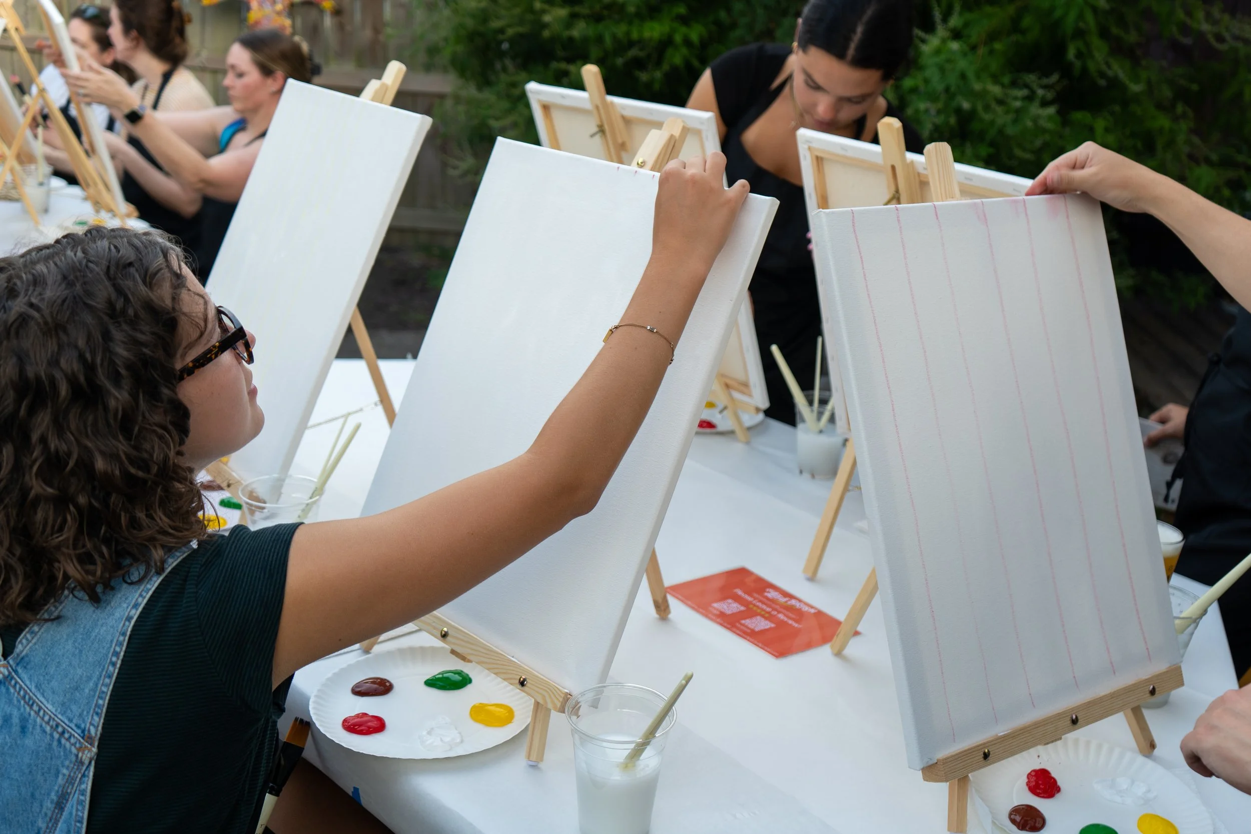 A girl with curly hair and glasses draws on a blank canvas with chalk