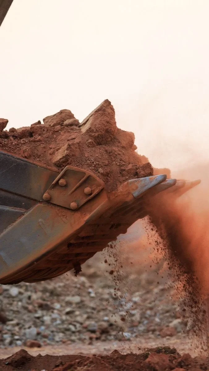 Close-up of a excavator bucket scoop filled with dirt and debris, with dirt falling off the edge.