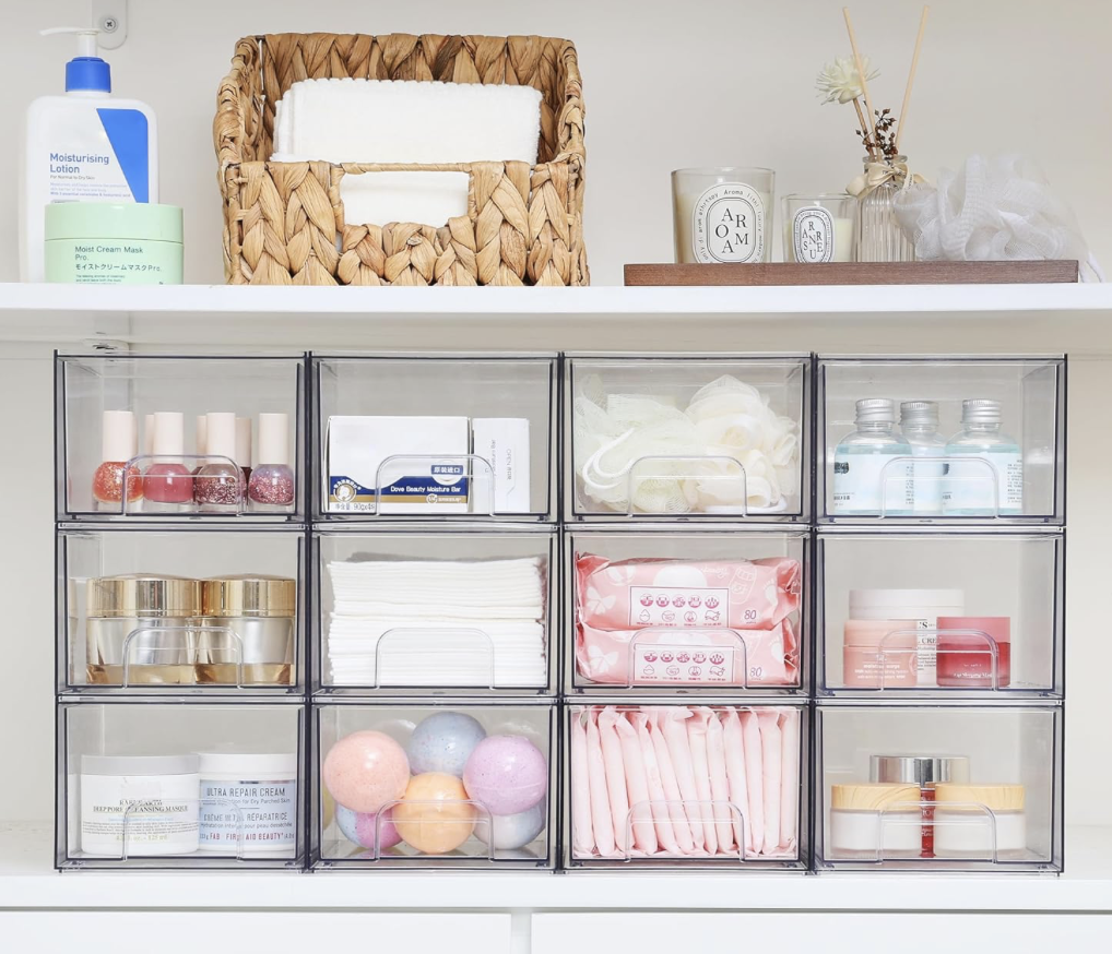 Organized skincare and beauty supplies in transparent storage boxes on a white shelf, including nail polish, cotton pads, face masks, skincare jars, cotton swabs, bath bombs, and tissues.