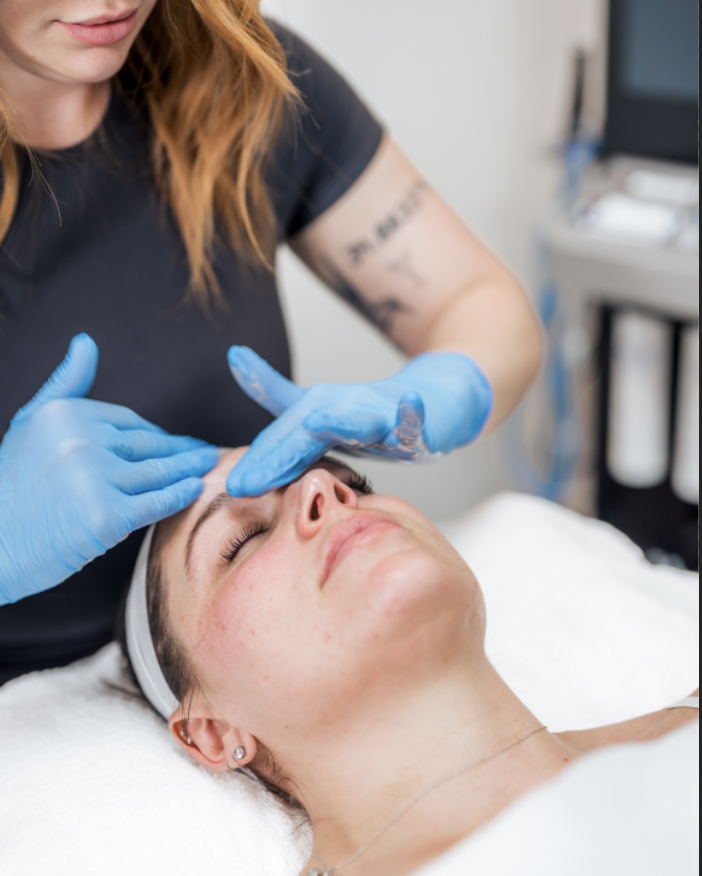 A woman receiving a facial treatment from a skincare professional wearing blue gloves in a clinic setting.