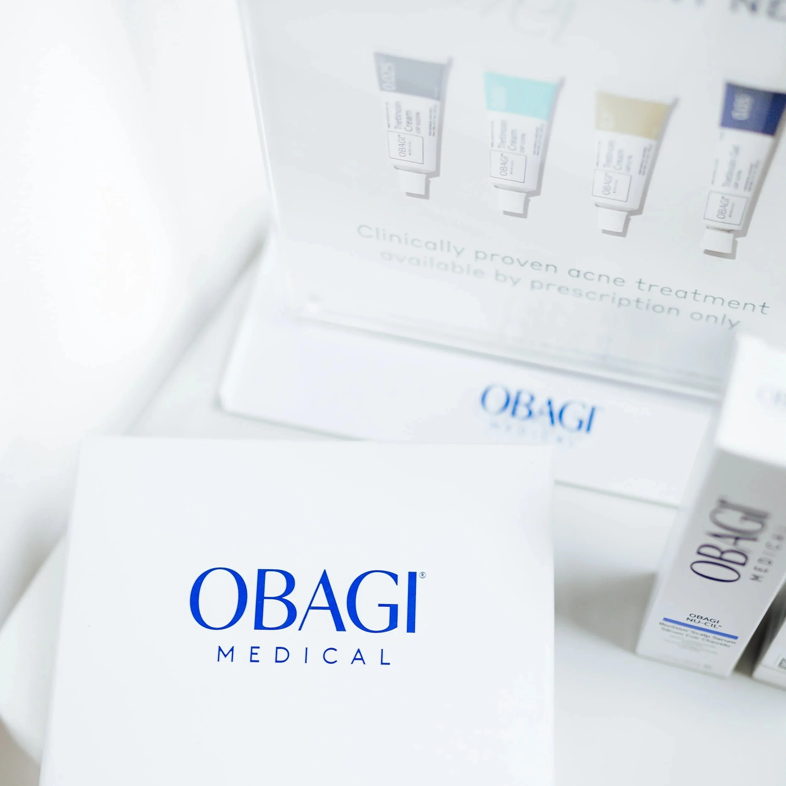 Close-up of OBAGI Medical skincare product packaging and promotional materials, including tubes of treatment cream and a box, displayed on a white surface.