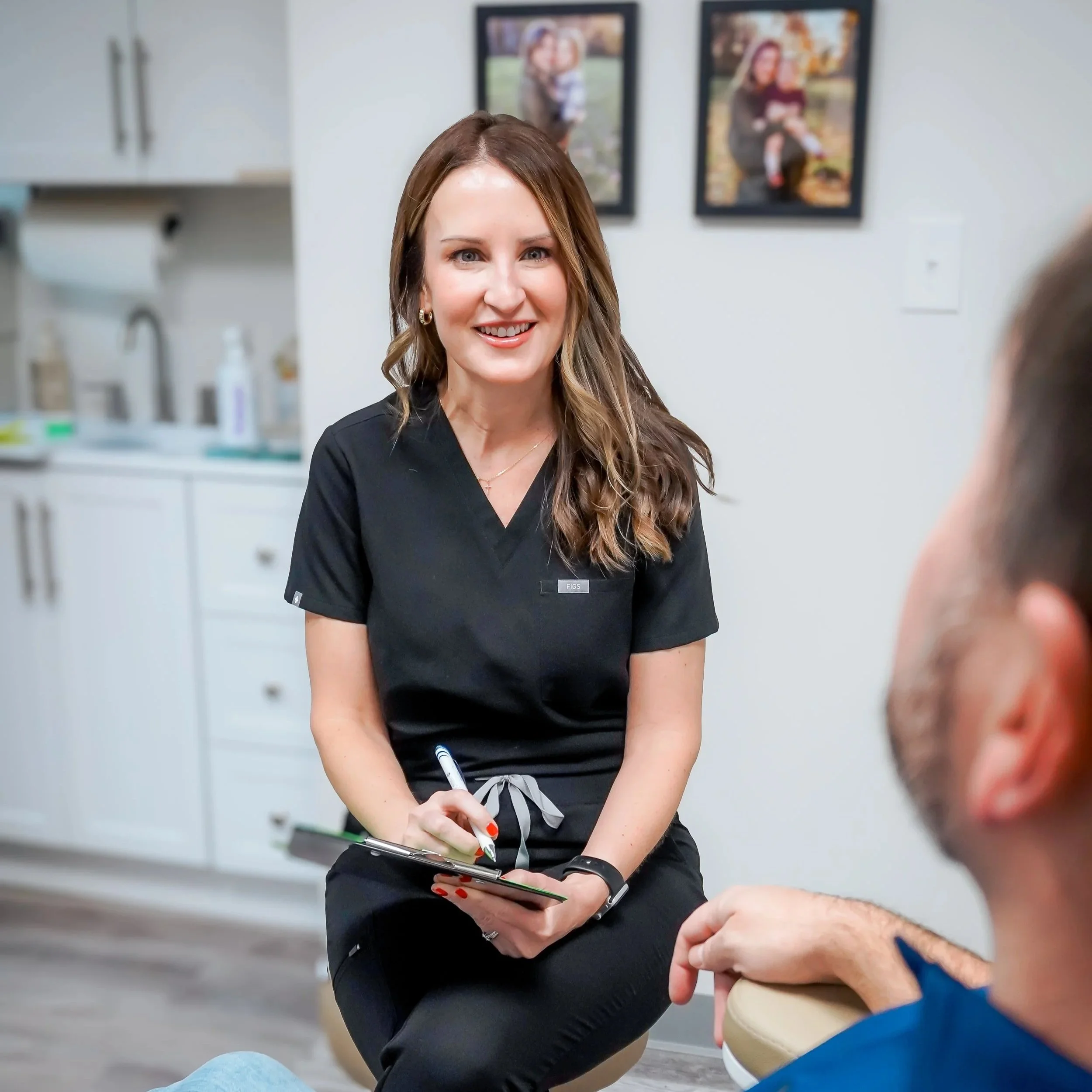 A woman in medical scrubs smiling and talking to a patient in an office or clinic setting for a wellness consultation including BHRT.