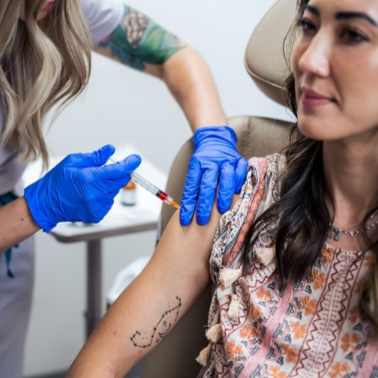 A woman receiving a vaccination shot from a healthcare professional wearing blue gloves.