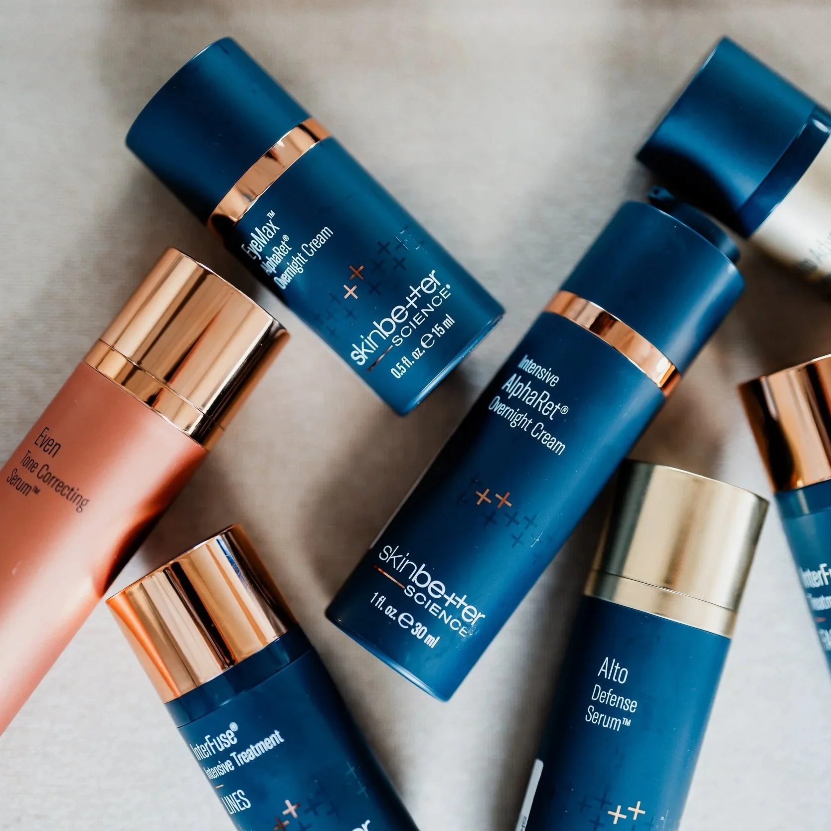 An assortment of skincare products in blue and gold bottles, including eye cream, night cream, serum, and treatment bottles, arranged on a neutral fabric background.