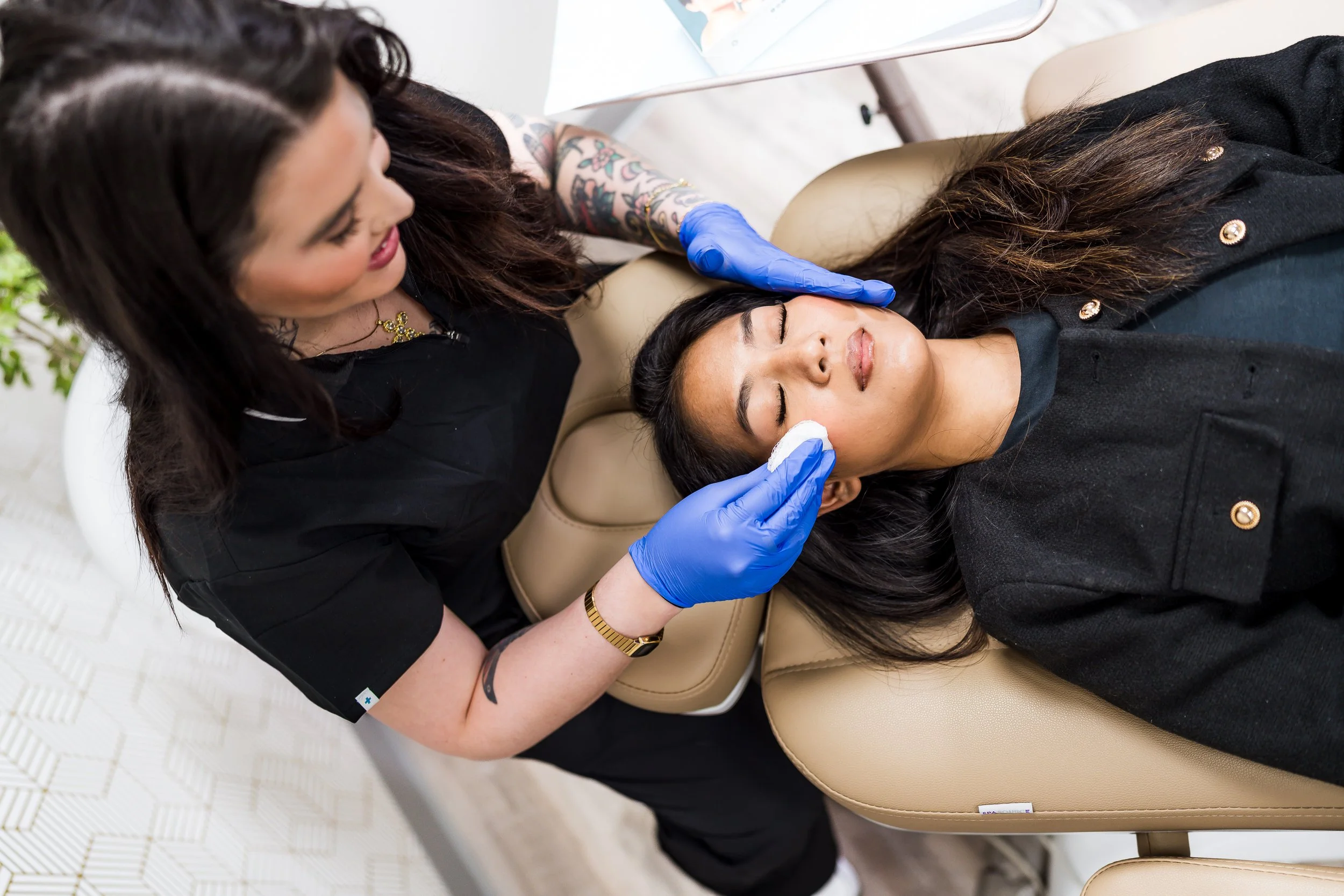 A woman receiving a cosmetic injection from a healthcare professional while lying on a beige medical chair.