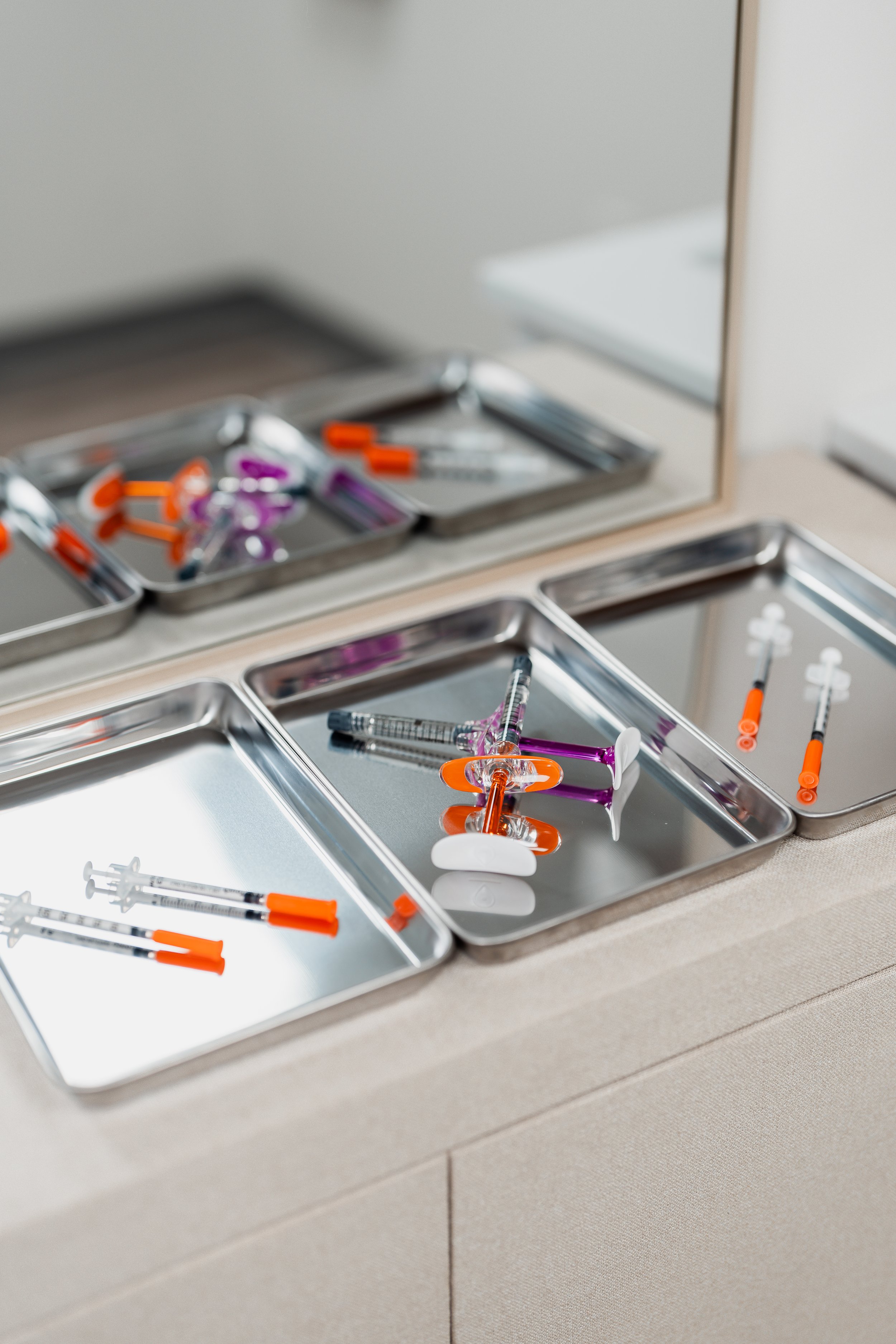 Medical syringes on stainless steel trays next to a mirror.