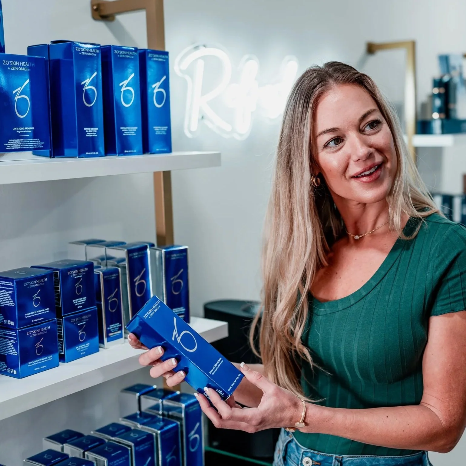 A woman shopping for skincare products inside a store, holding a blue box labeled ZO Skin Health, with shelves stocked with similar blue boxes in the background.