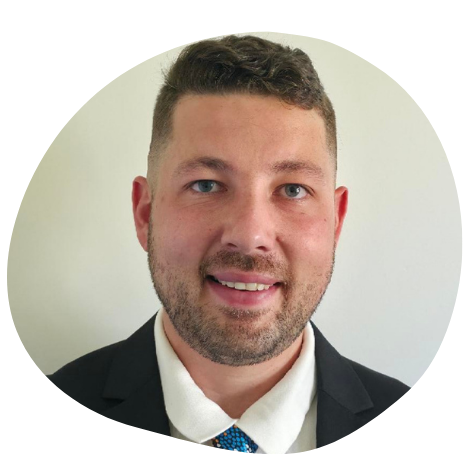 A smiling man with short brown hair and a tie and a light background.
