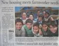 Group of children smiling, holding a large check, in front of a building, news headline about housing and farmworker needs.