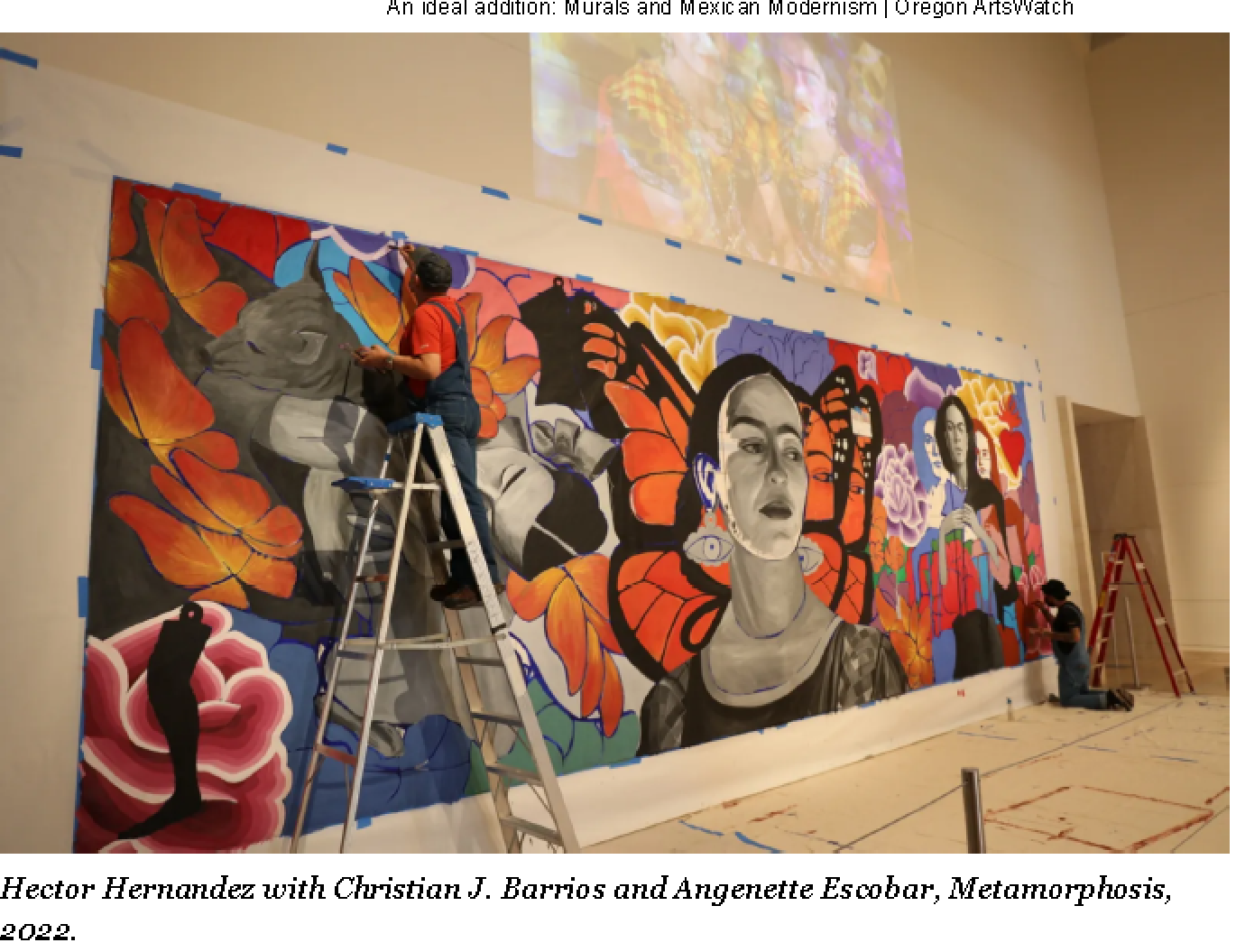 Three people working on a large mural with vibrant and detailed portraits of women and colorful floral and butterfly patterns. Two are on ladders, painting, while one stands on the floor.