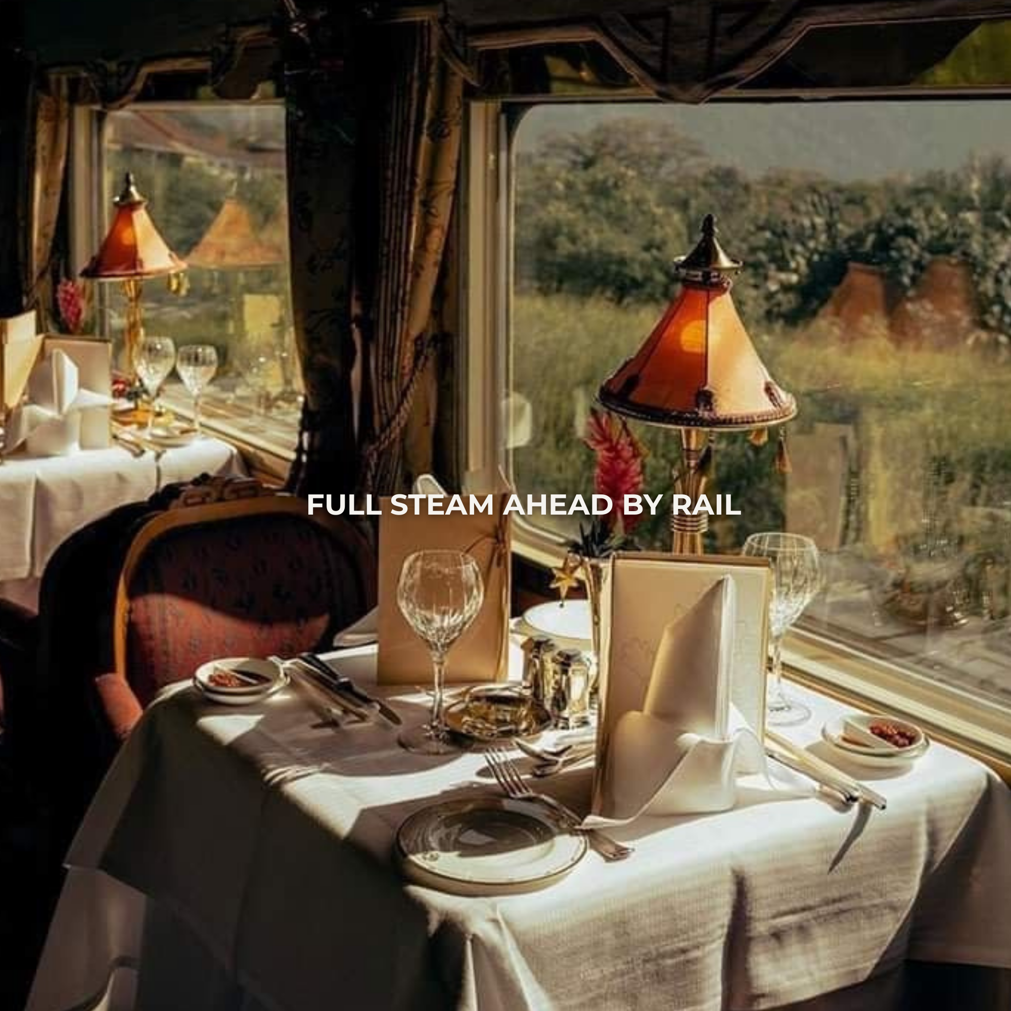 Restaurant dining table set with white tablecloth, wine glasses, folded napkins, and a small lamp, near large windows showing a scenic outdoor view.