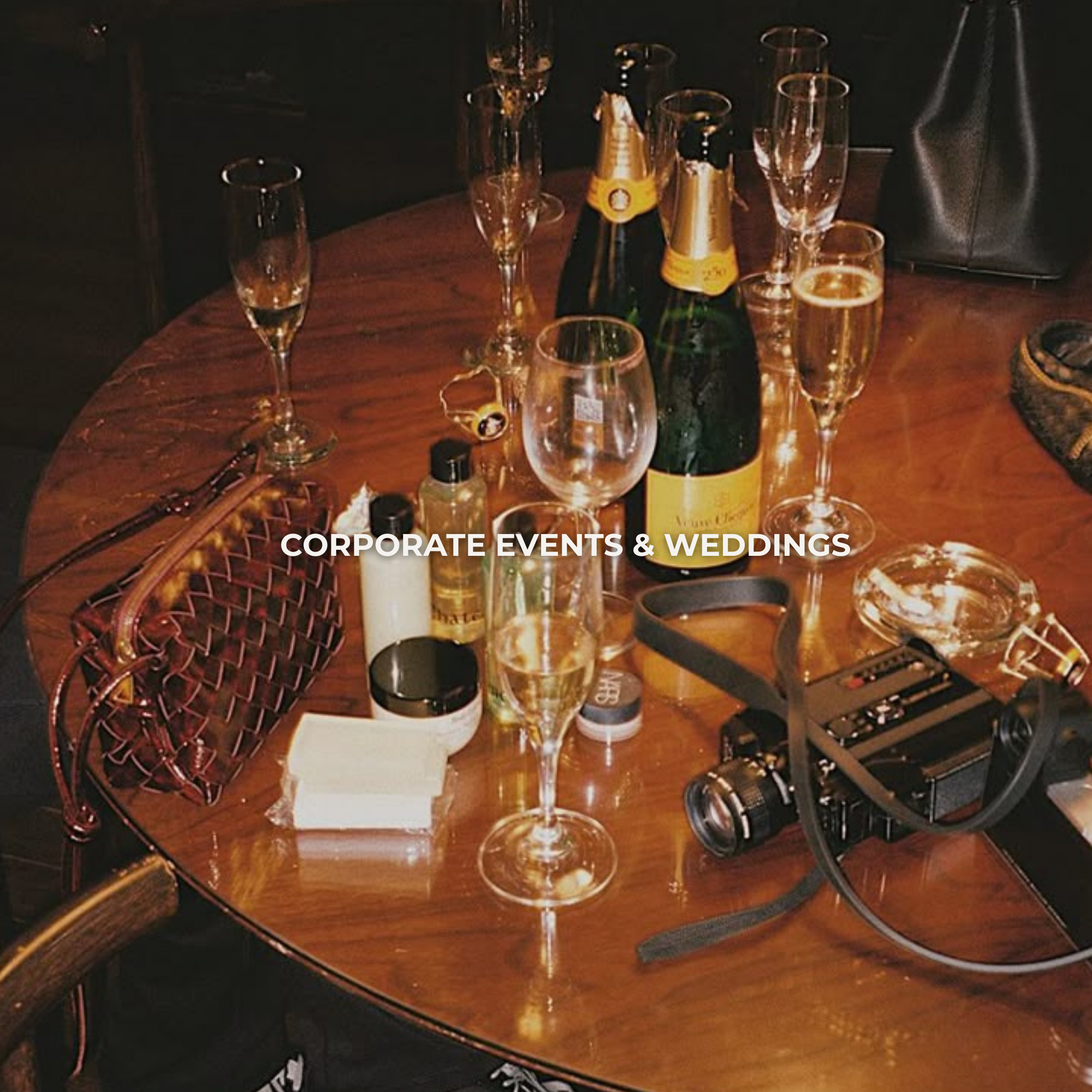 A round wooden table with empty champagne glasses, bottles of champagne, a camera, a purse, a candle, and some small items, set for a celebration or event.