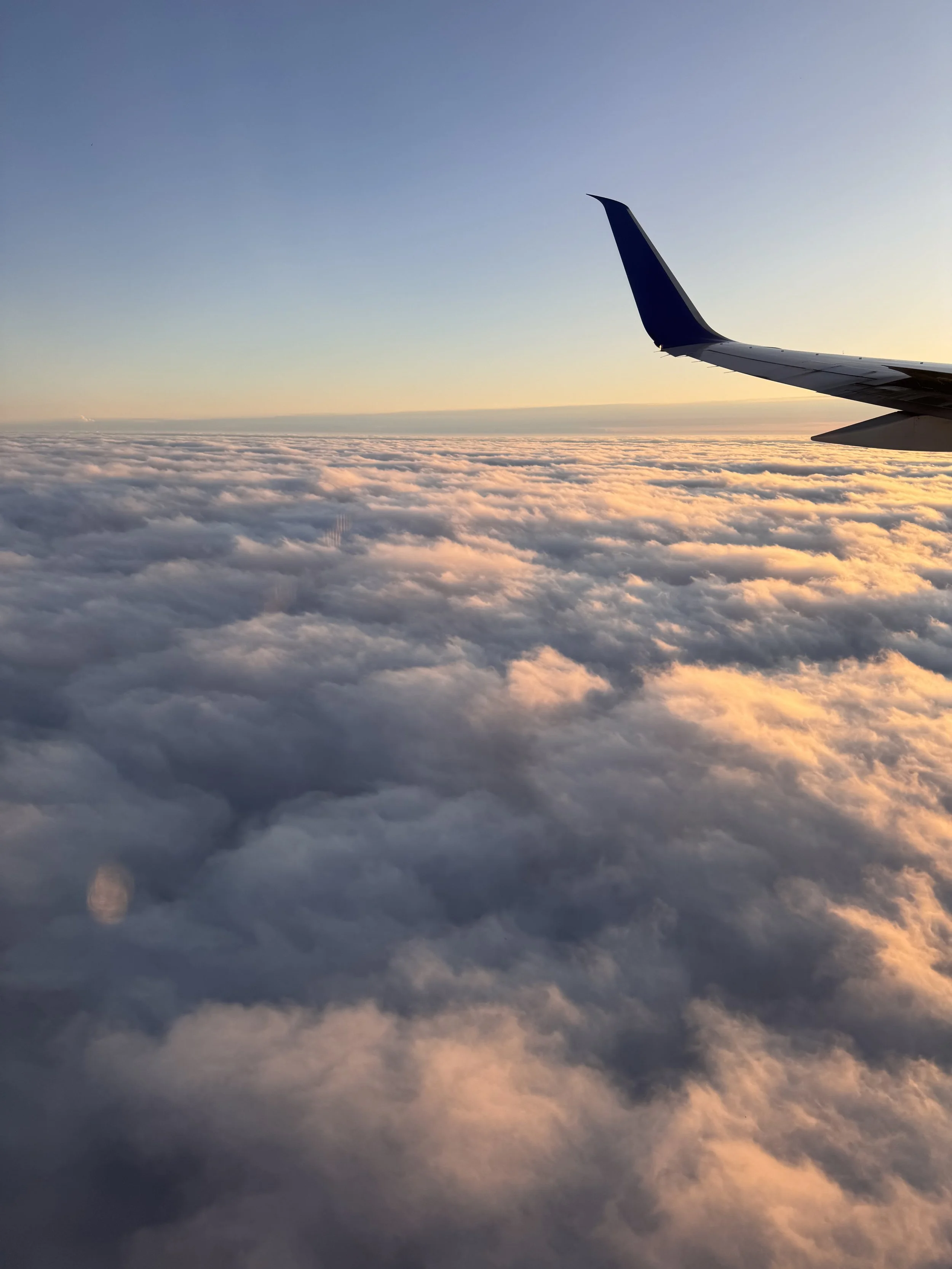 View outside an airplane window showing clouds and a clear sky during sunset or sunrise.