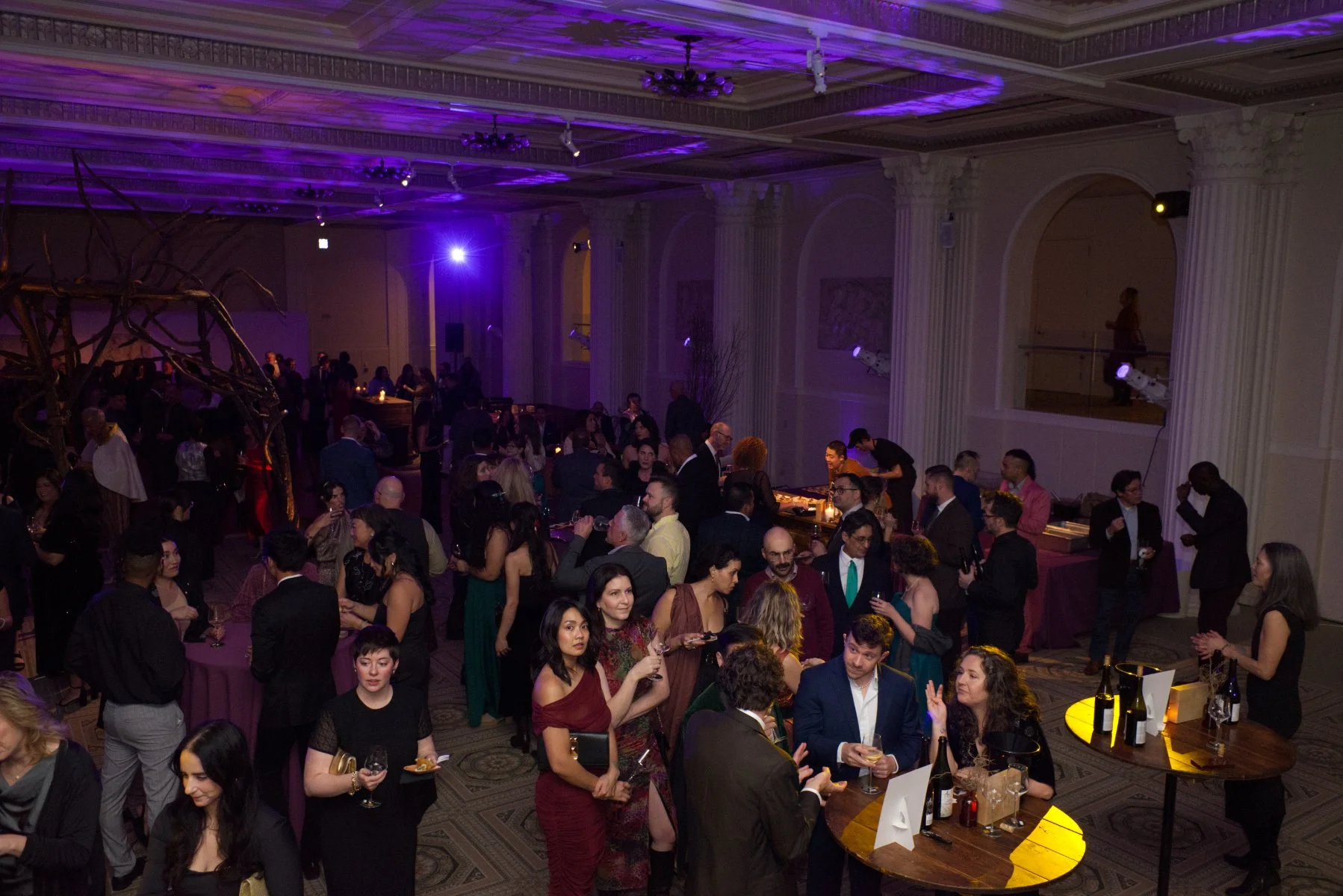 Guests mingling and socializing at a formal event in a large, decorated ballroom with purple lighting.