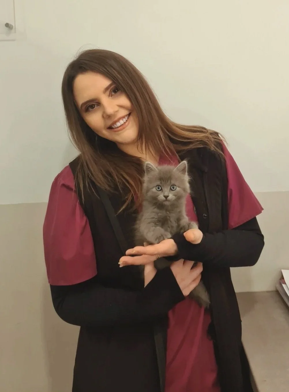 A smiling woman with natural curly hair, glasses, hoop earrings, layered necklaces, and a striped blouse.