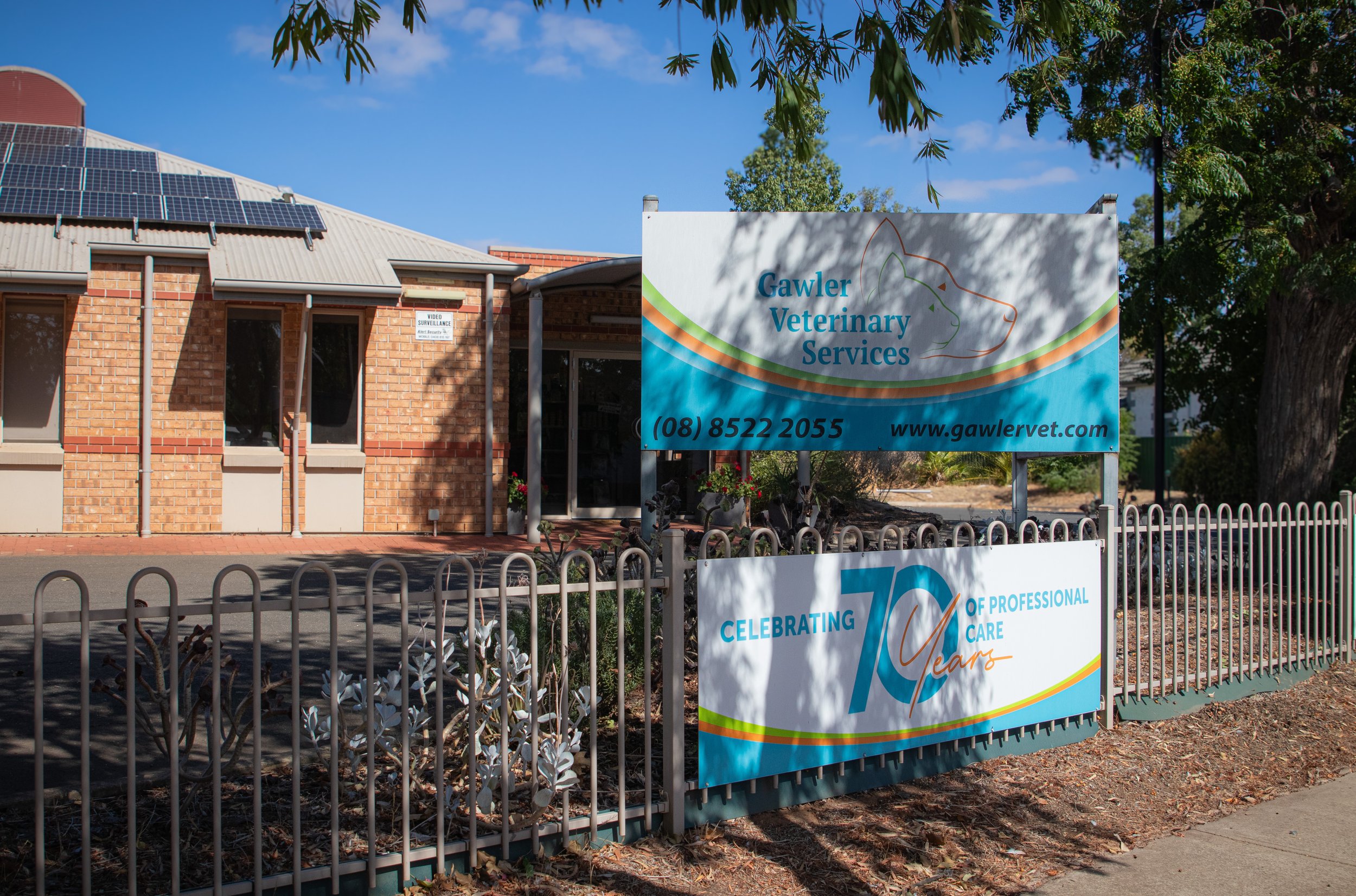 Sign for Gawler Veterinary Services in front of a brick building with solar panels on the roof, surrounded by a fence and trees.
