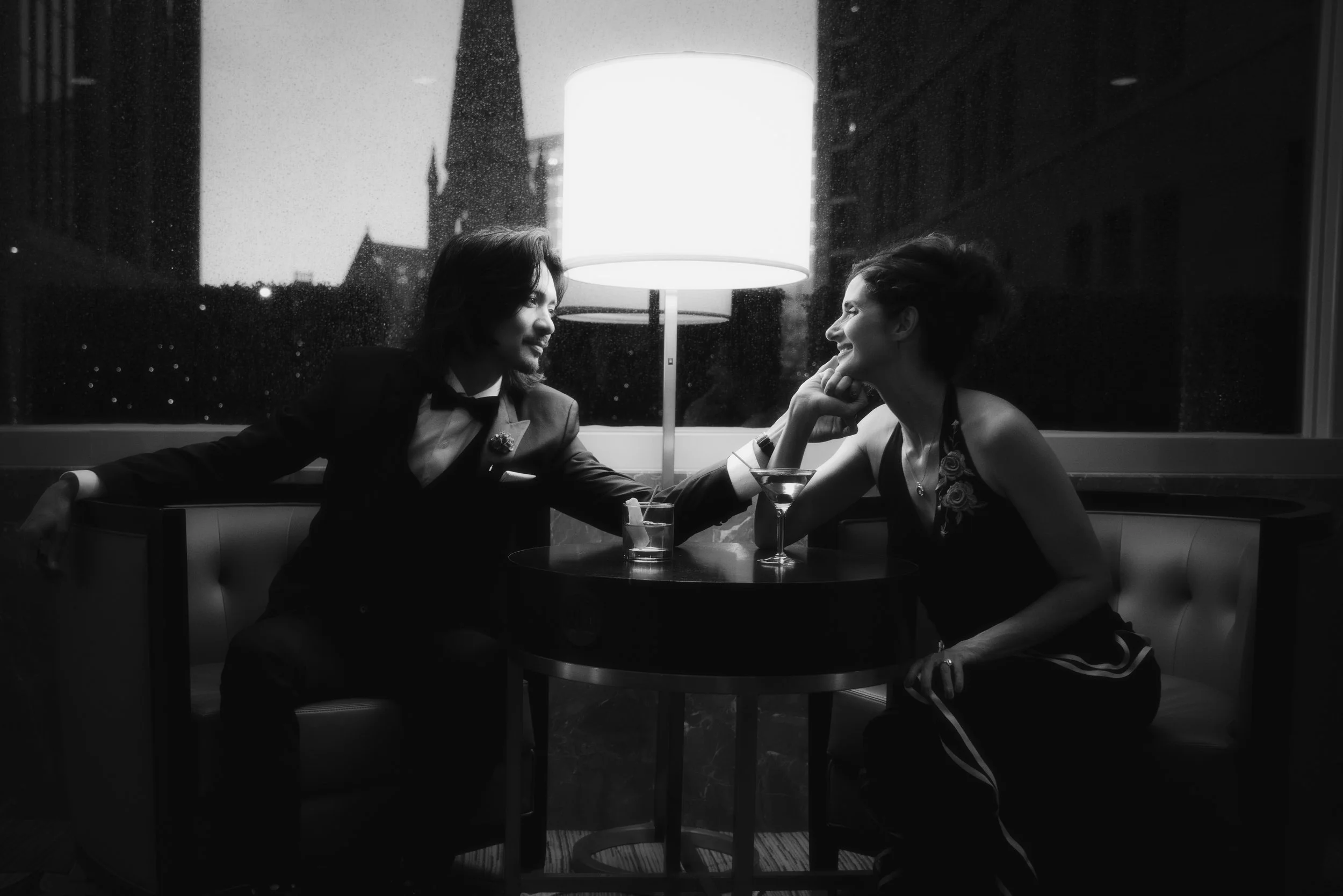 A couple looking longingly at one another across a bar room table with a lamp in between them, softly casting a light on their faces.  The groom is caressing his brides cheek and she is smiling back at him.  They just eloped in Denver, Colorado.