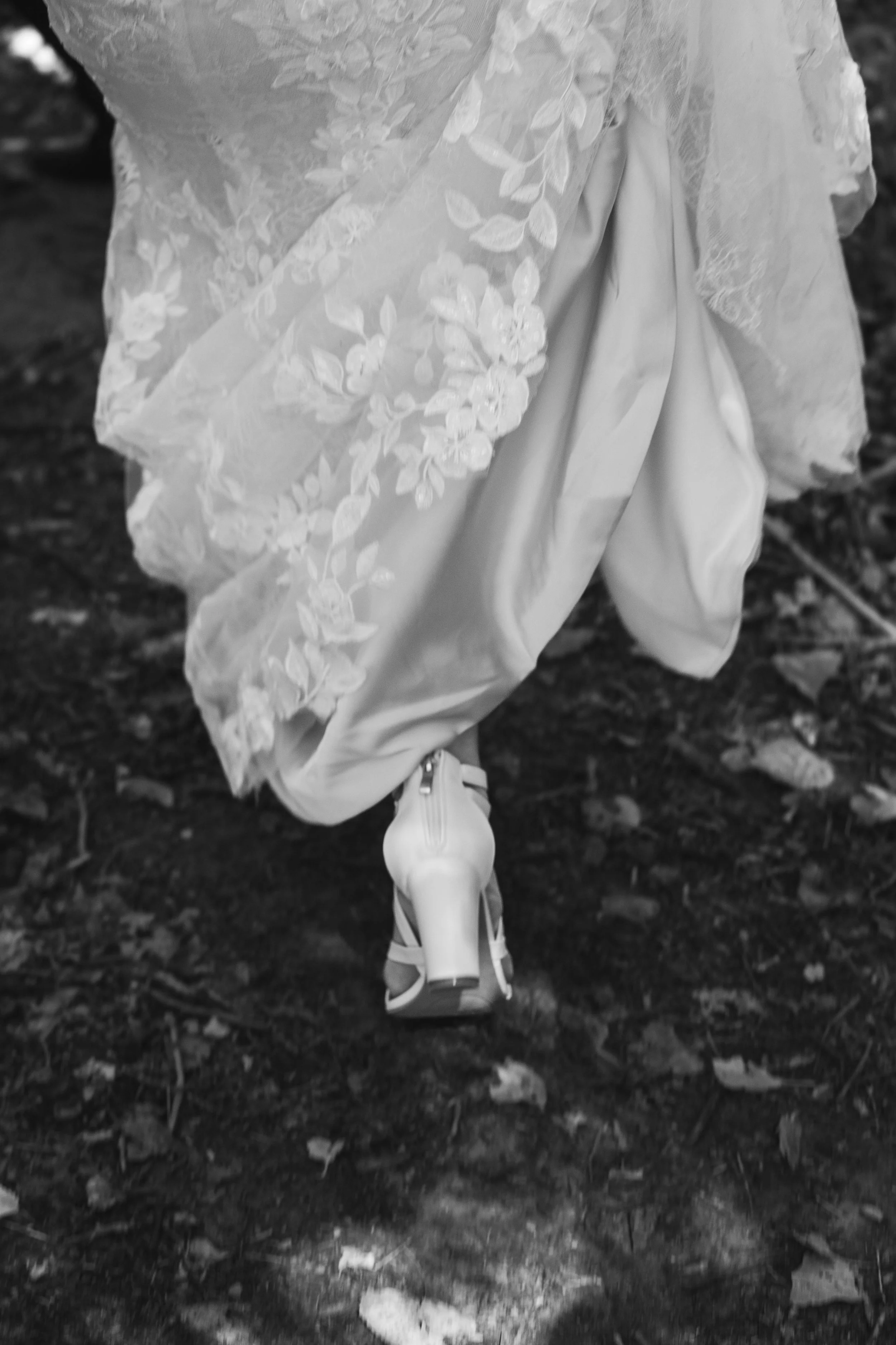 A stylized photo of a bride's shoe while she is walking forward on a dirty trail.  She's clearly holding her dress up with one hand, her bouquet in the other.  This photo could be taken anywhere, but it resembles any womens' wild beauty.