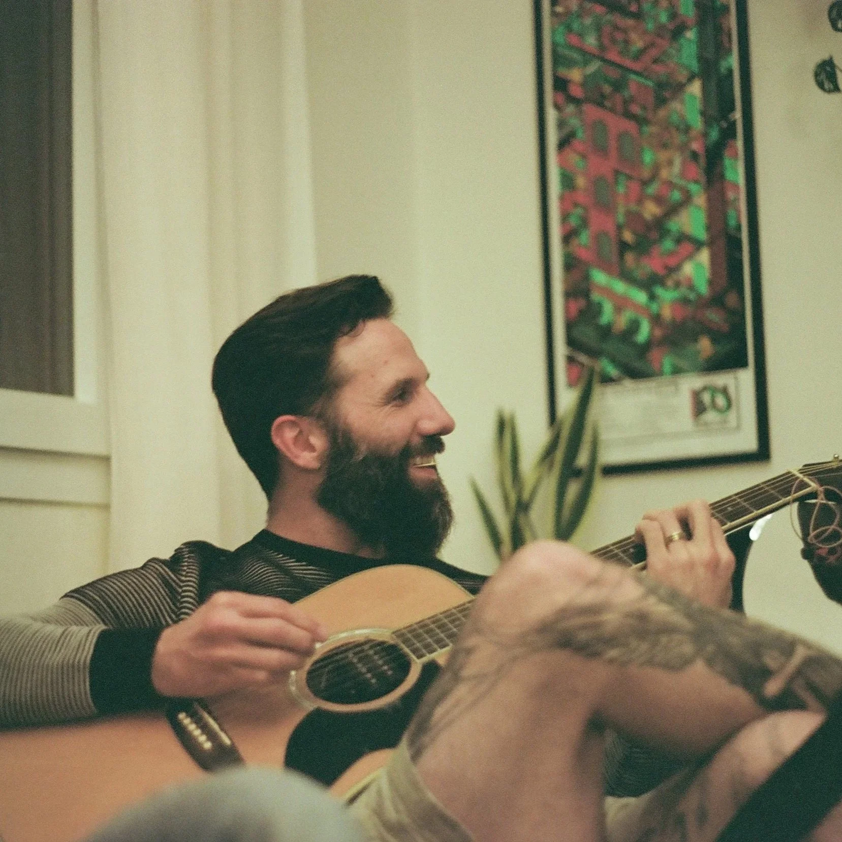Underneath a portion of the page describing Pauls love for music, a candid film photo of him shows him laughing with friends and playing an acoustic guitar in a living room.   This shows how music is involved in his daily life.